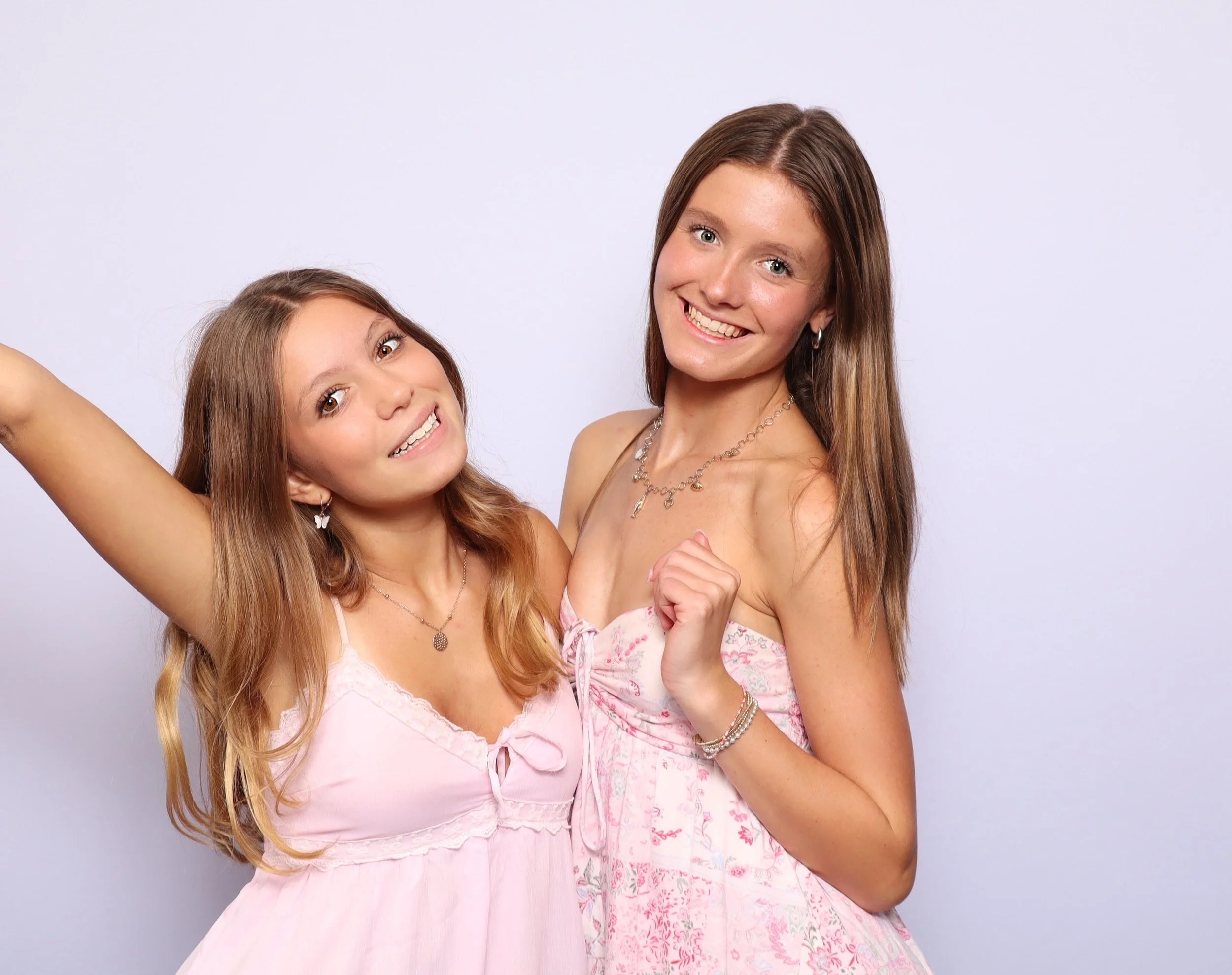 Two young women in pink dresses smiling and posing against a plain background.