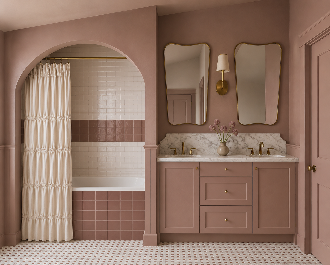 A bathroom featuring a double vanity with pink cabinetry, marble countertops, and two gold faucets. Above the vanity are two irregularly shaped mirrors with gold frames, and a wall-mounted gold light fixture. A vase with pink flowers sits on the countertop. To the left, a bathtub is partially visible behind a cream shower curtain with an arched opening, pink and white tile walls, and patterned tile flooring.
