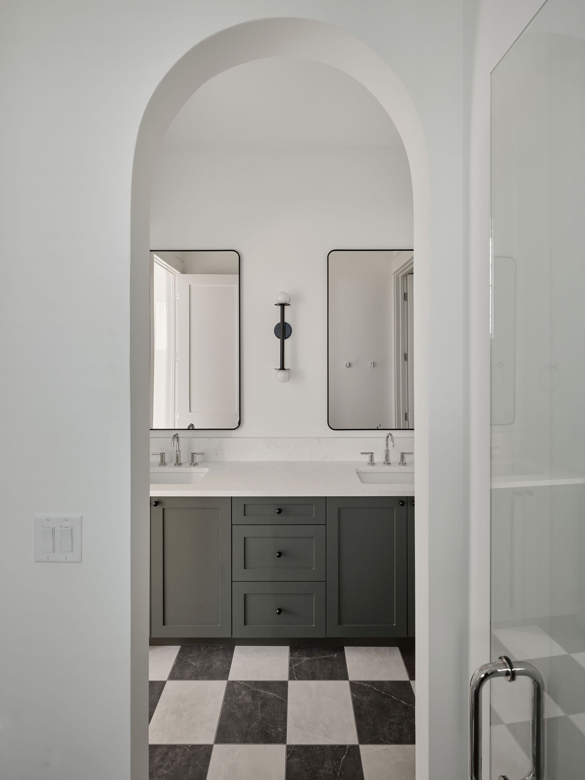 Bathroom with double sink vanity, green cabinets, white countertop, mirror, and black and white checkered tile floor.