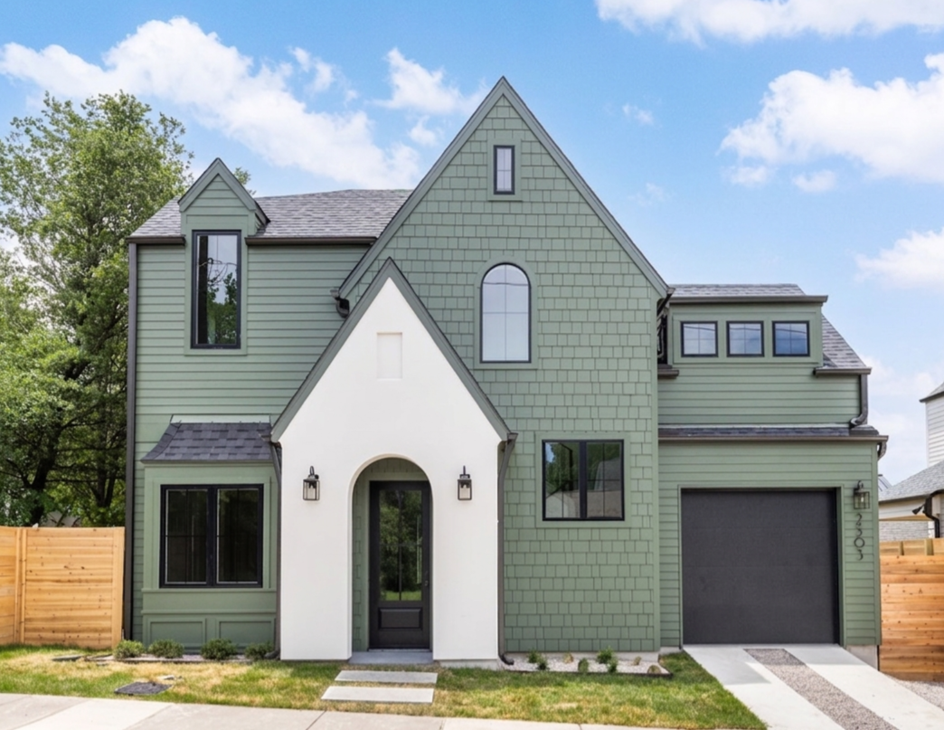 Modern house with multiple gabled roofs, a white arched entryway, and large windows, surrounded by a green lawn and trees in the background.