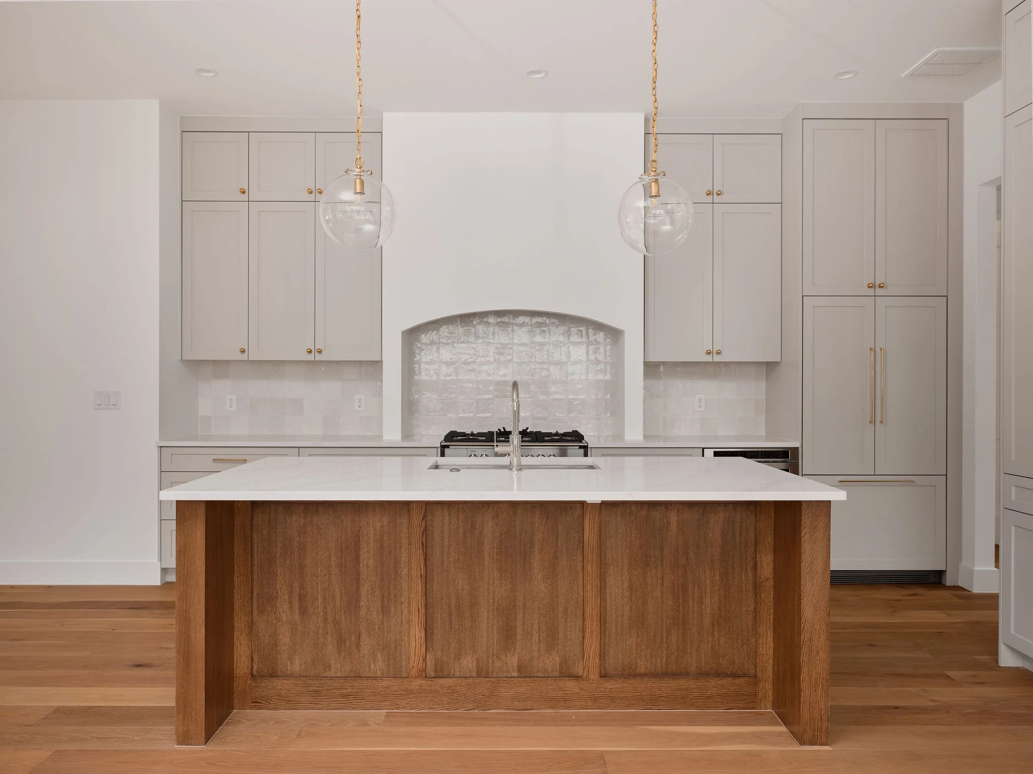 Modern kitchen with white cabinets, a central island with a wooden finish, pendant lights, and a white tiled backsplash.