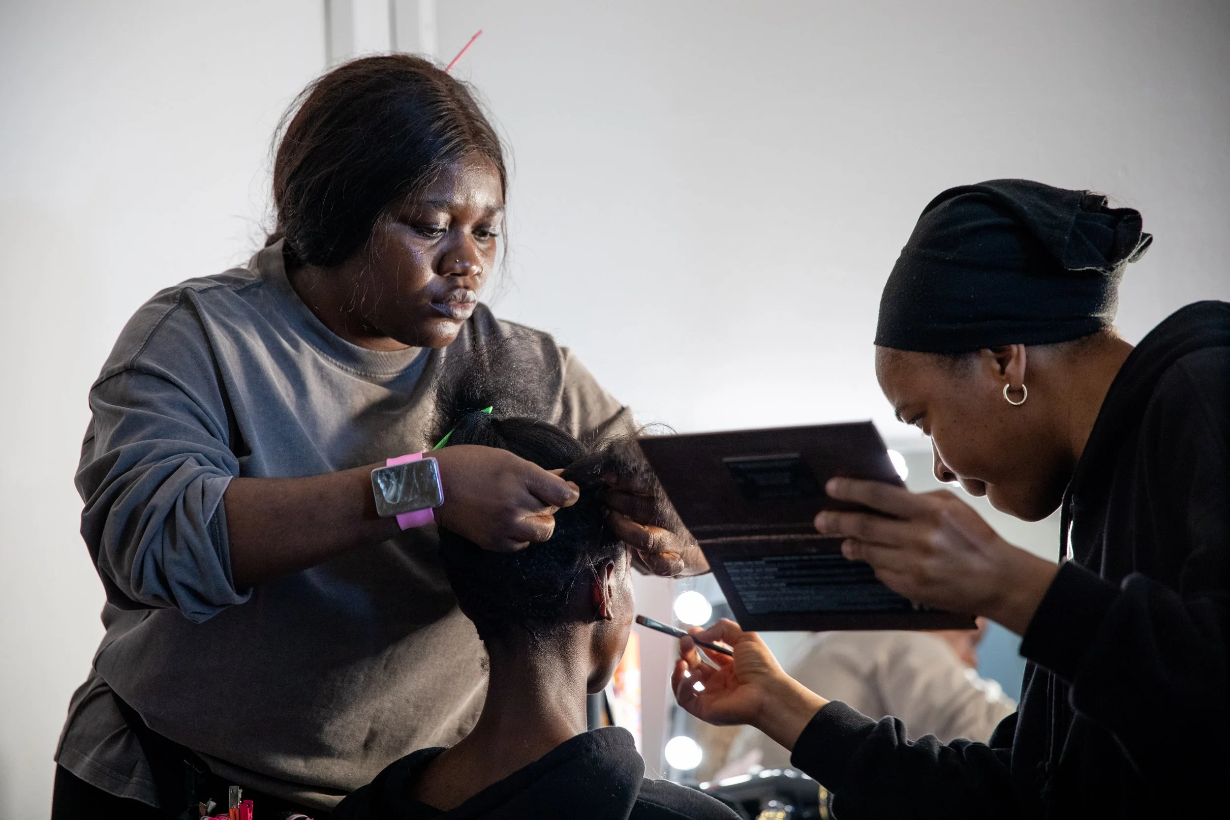Two women and a girl are engaged in a beauty or hair treatment, with the women focusing on the girl's hair, in a well-lit indoor space.
