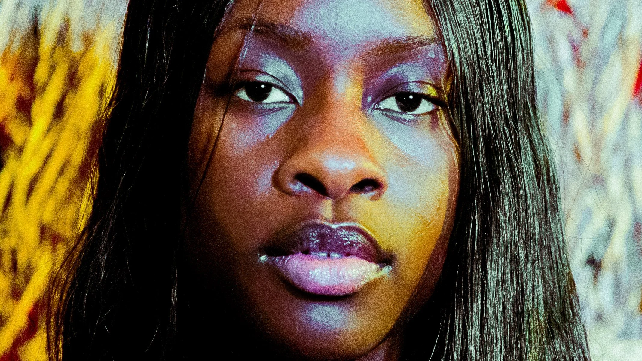 Close-up of a woman with long black hair, wearing eye makeup, pink lipstick, and looking directly at the camera.