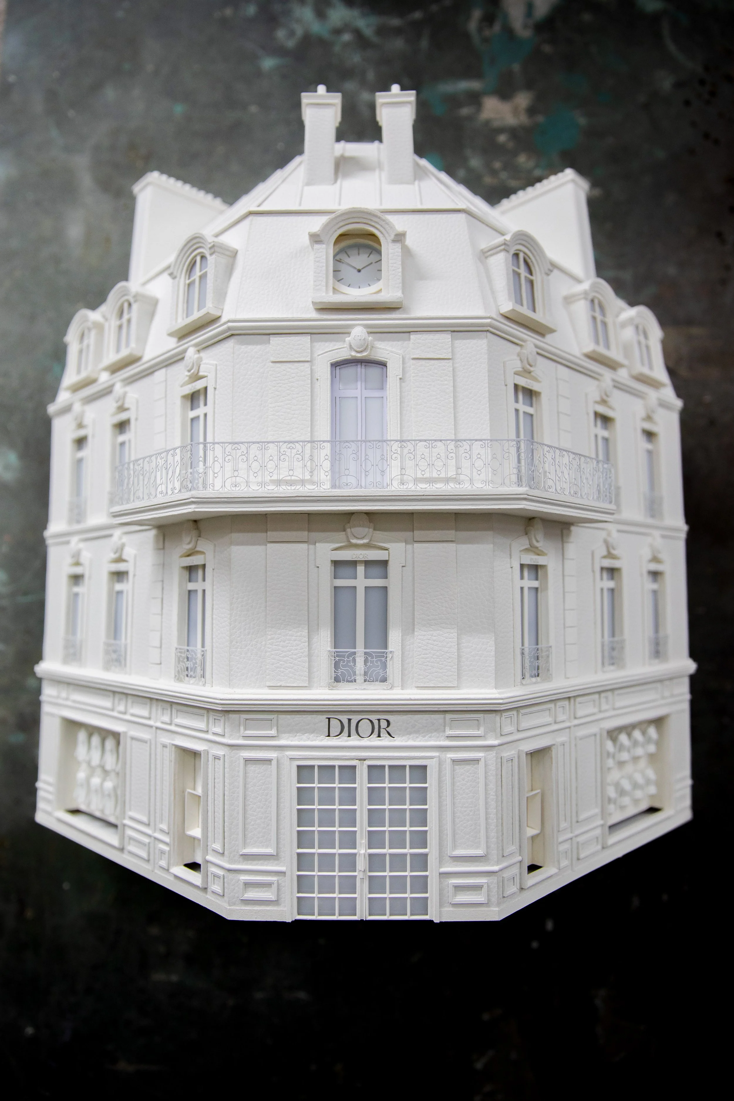A detailed white scale model of a multi-story building with classic architecture, including decorative balconies and a clock on the roof, labeled 'DIOR'.