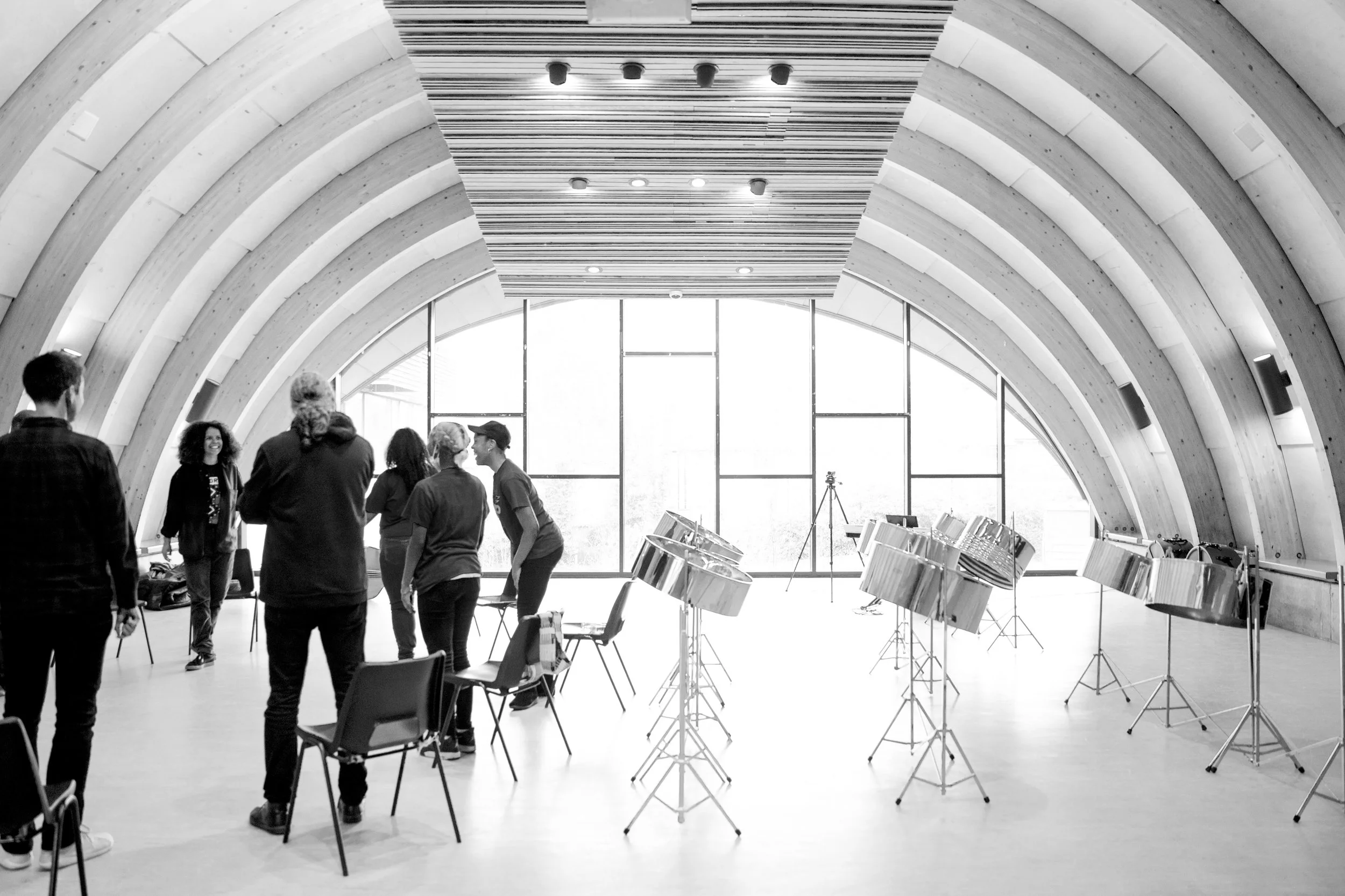 People standing and talking in a modern, curved architectural space with wooden arches, large windows, and musical stands.
