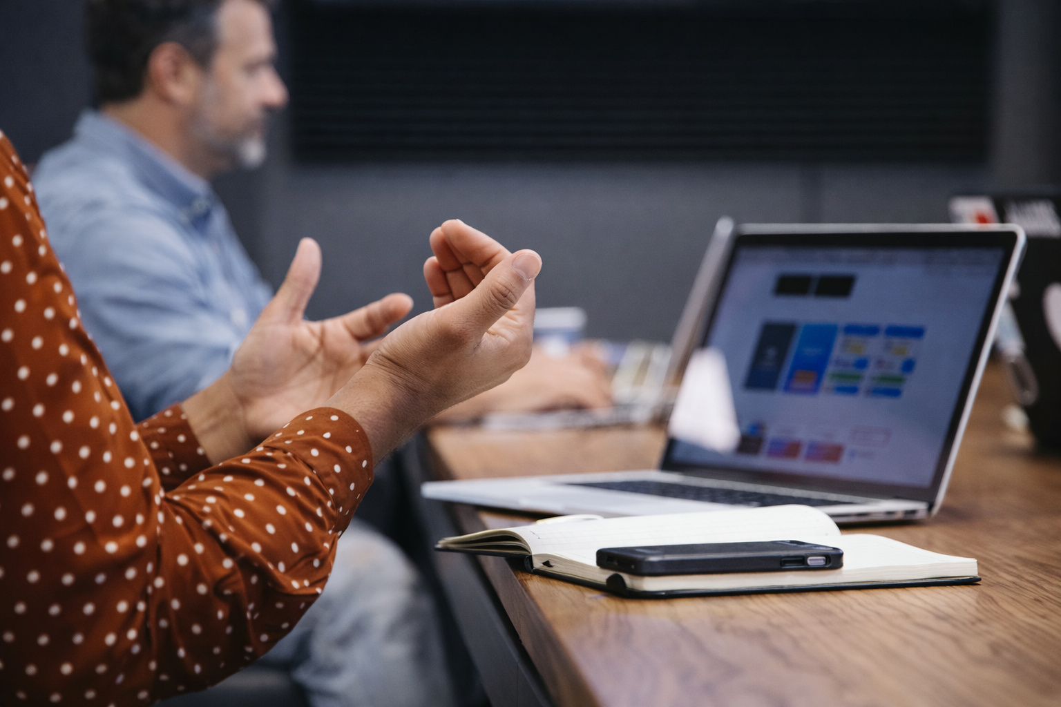 People in a meeting or discussion, with laptops, notebook, and smartphone on the table.