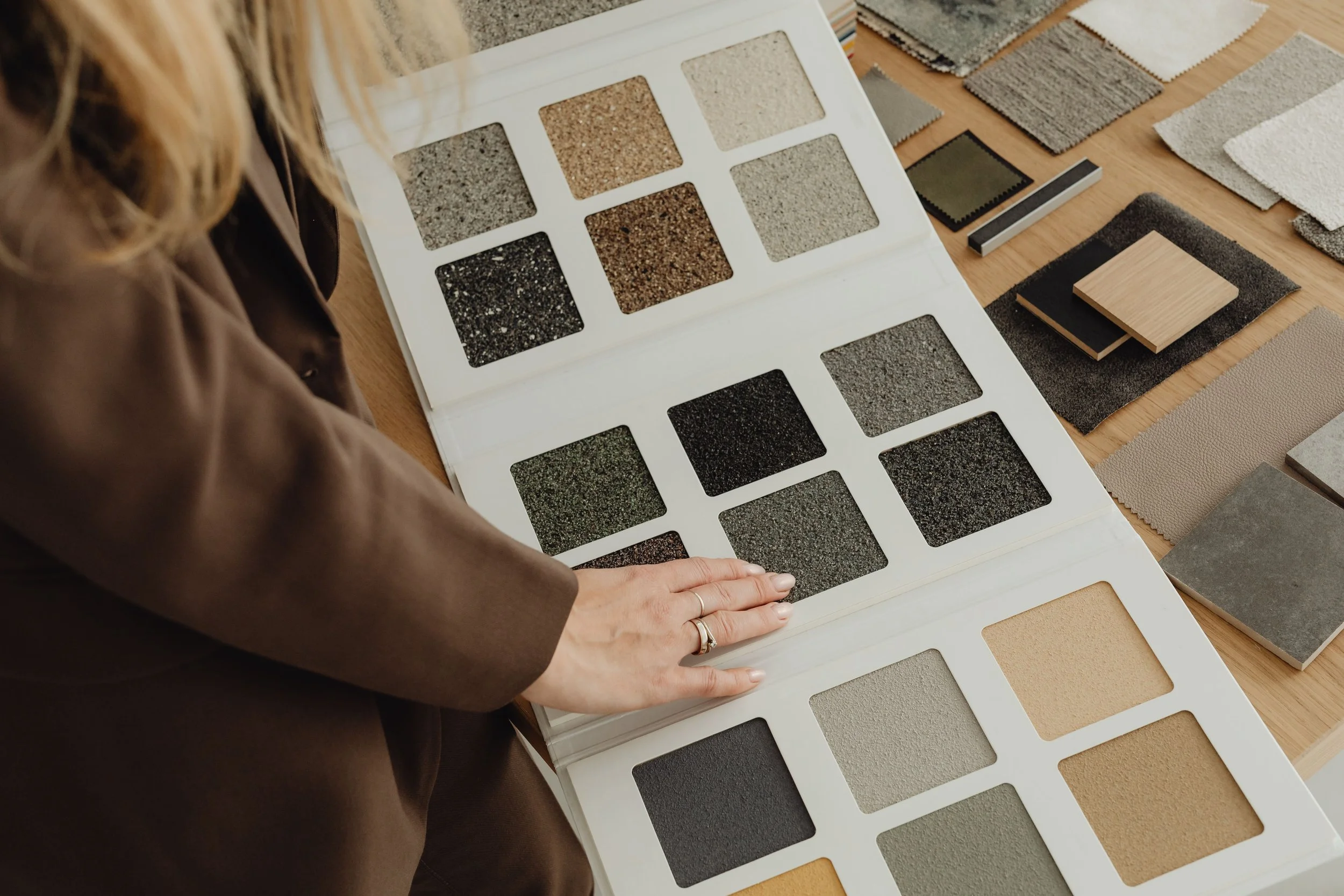 Frau betrachtet Musterkatalog mit verschiedenen Plättchen für Boden- oder Wandbeläge in einem Raum.