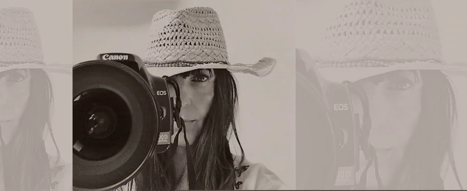 Eine Frau trägt einen Strohhut und fotografiert mit einer Canon EOS Kamera.