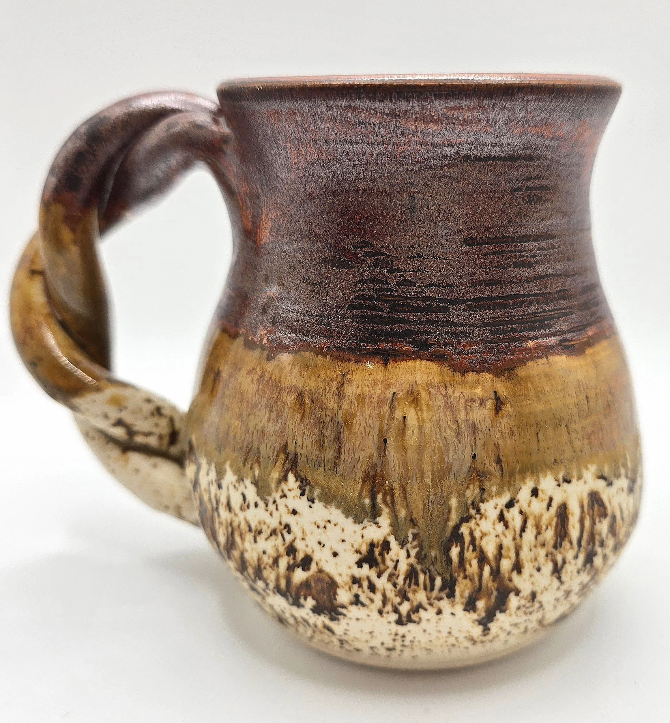 Close-up of a handmade ceramic mug with a brown and cream glaze and textured finish.