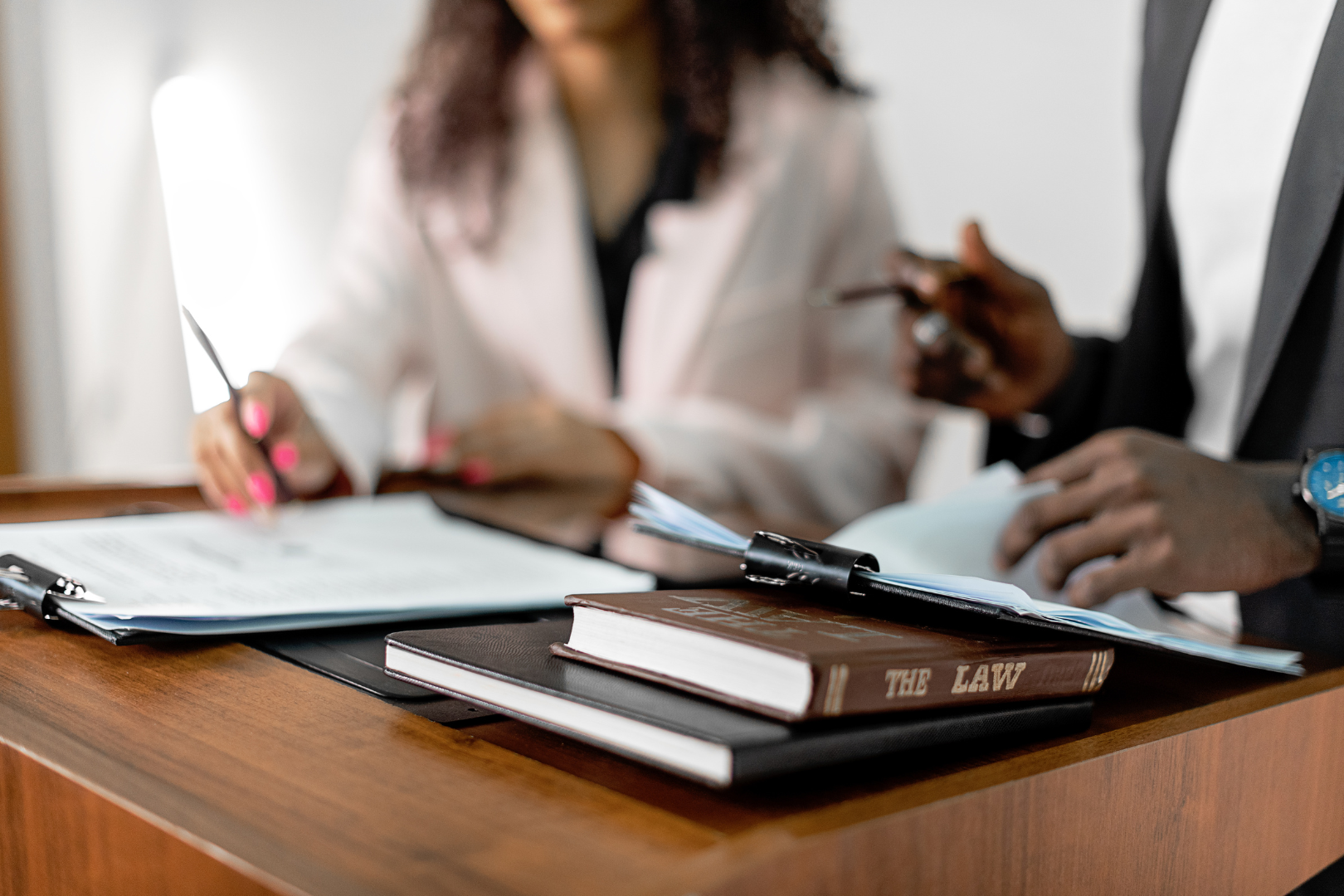 Two lawyers sitting at a wooden table reviewing legal documents, with a law book titled "The Law" in the foreground.