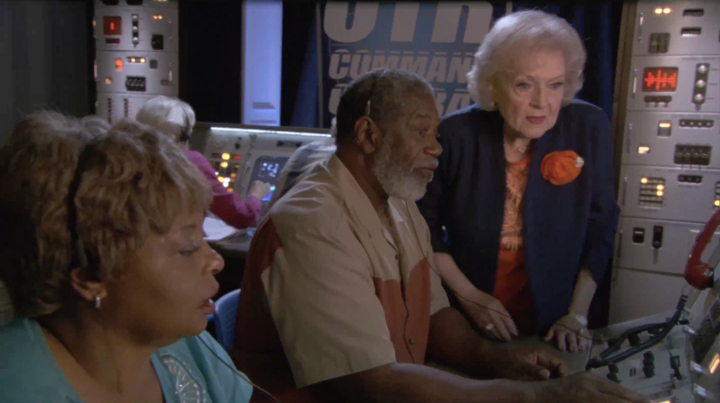 Group of people in a command center with control panels and headsets.