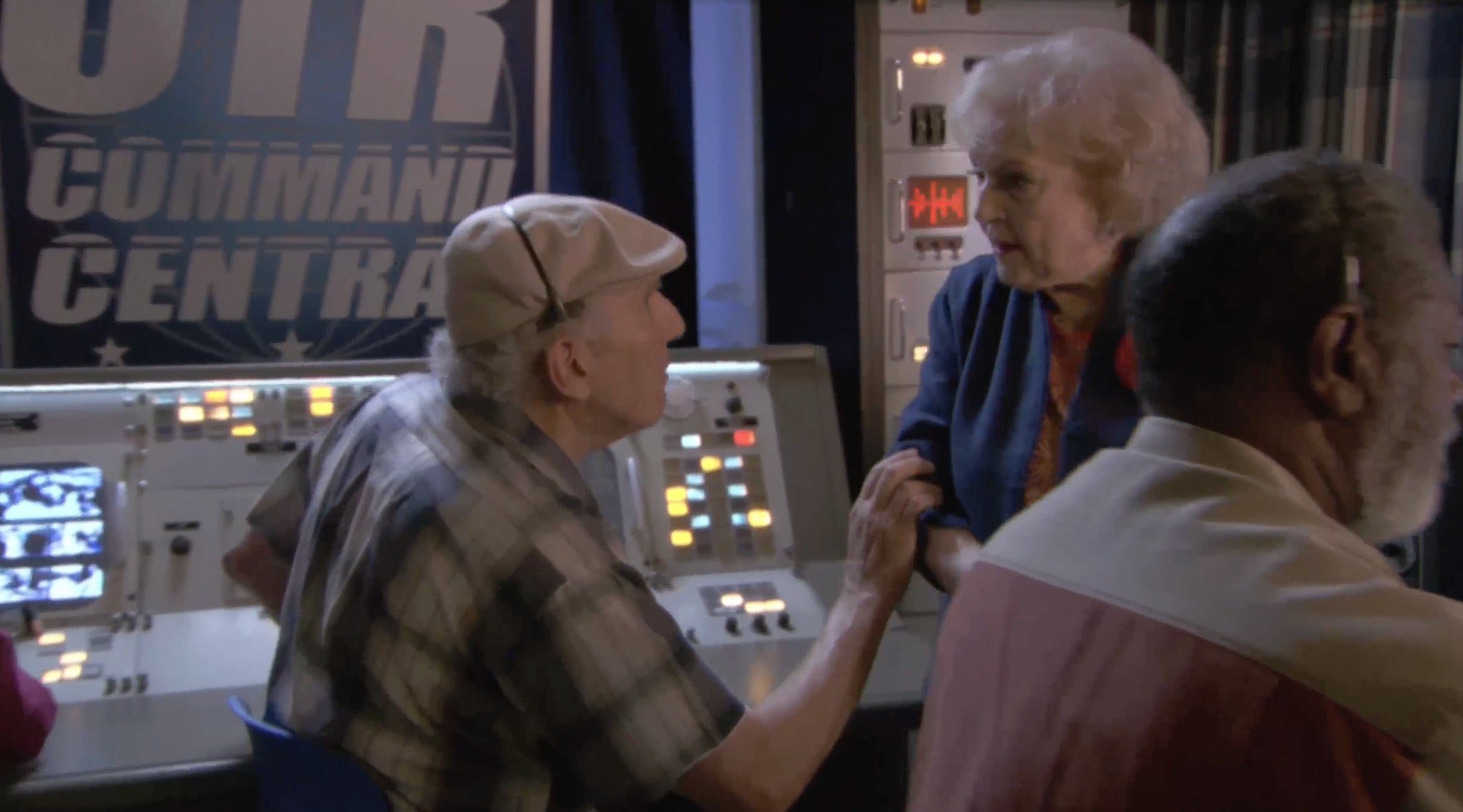 Three people in a control room with electronic equipment and a "Command Central" sign
