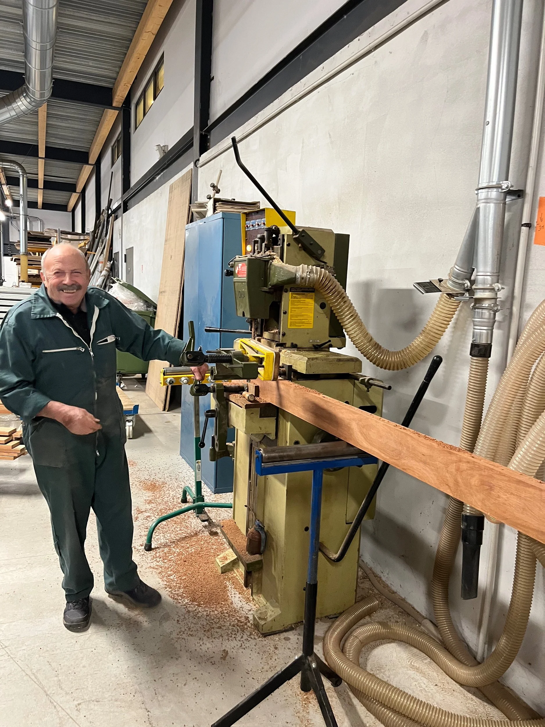 Homme souriant utilisant une machine à bois dans un atelier de menuiserie.