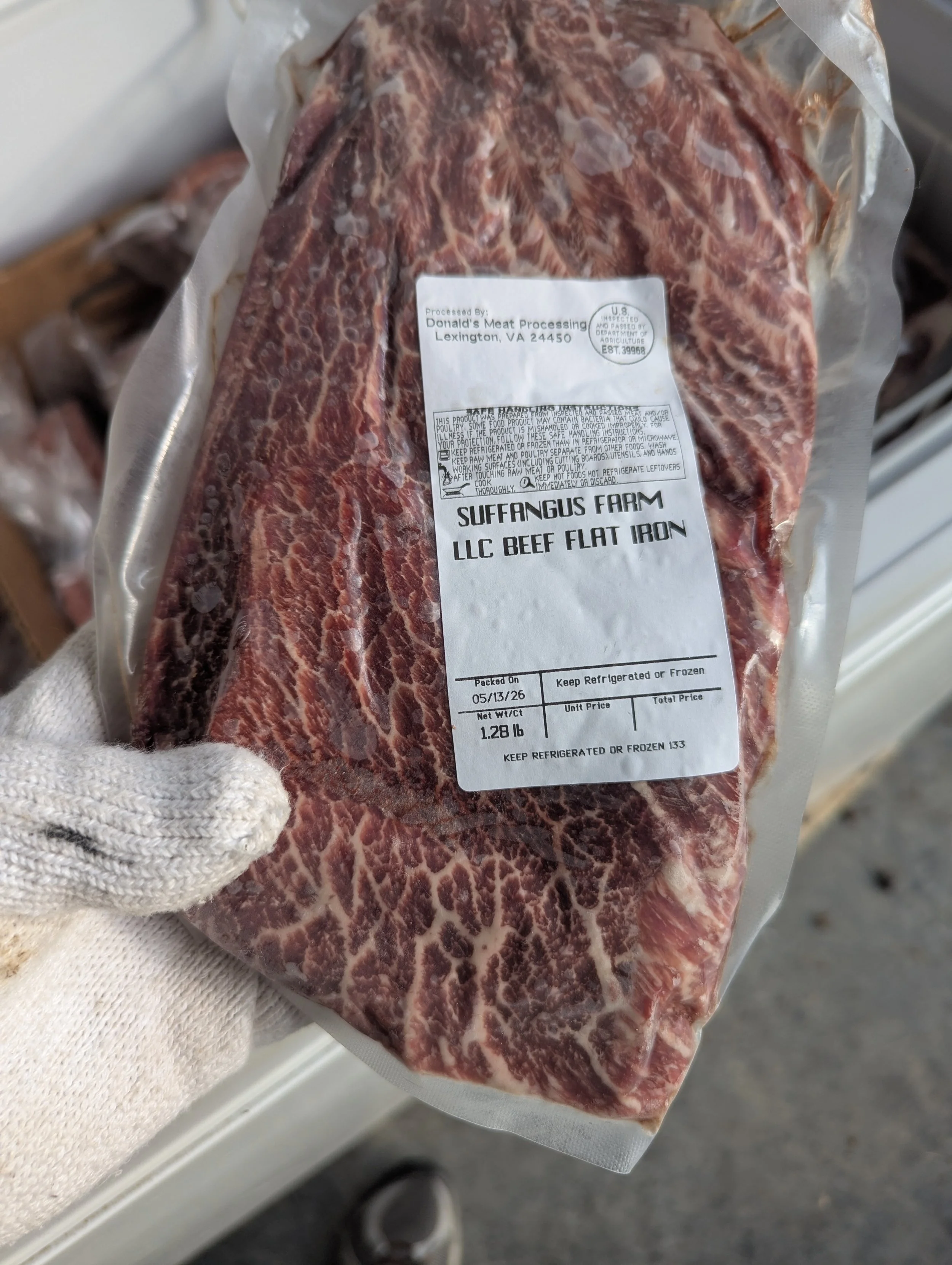 A package of raw beef flat iron steak with marbling, labeled from Suffangus Farm, USDA inspected, in a vacuum-sealed plastic bag.