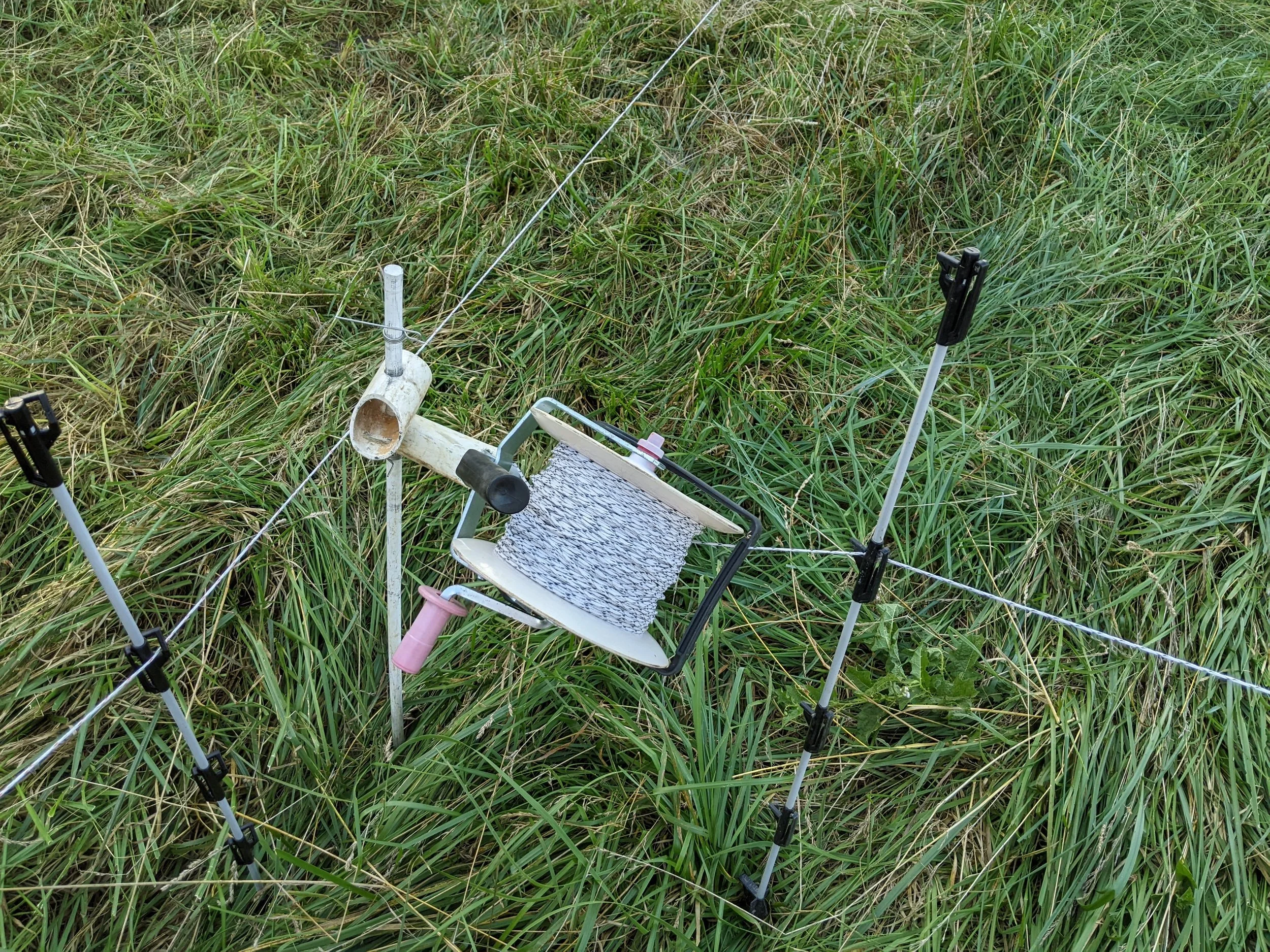 A field of tall grass with a small equipment setup, including a chair, some poles, and a caliper, used for wildlife monitoring or research.