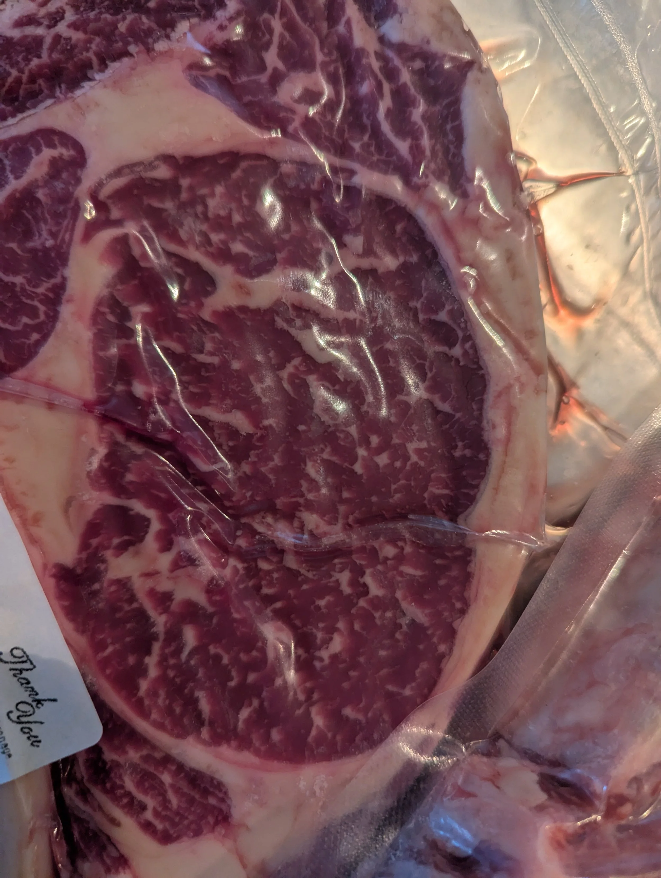 A piece of raw marbled beef steak sealed in clear vacuum packaging.