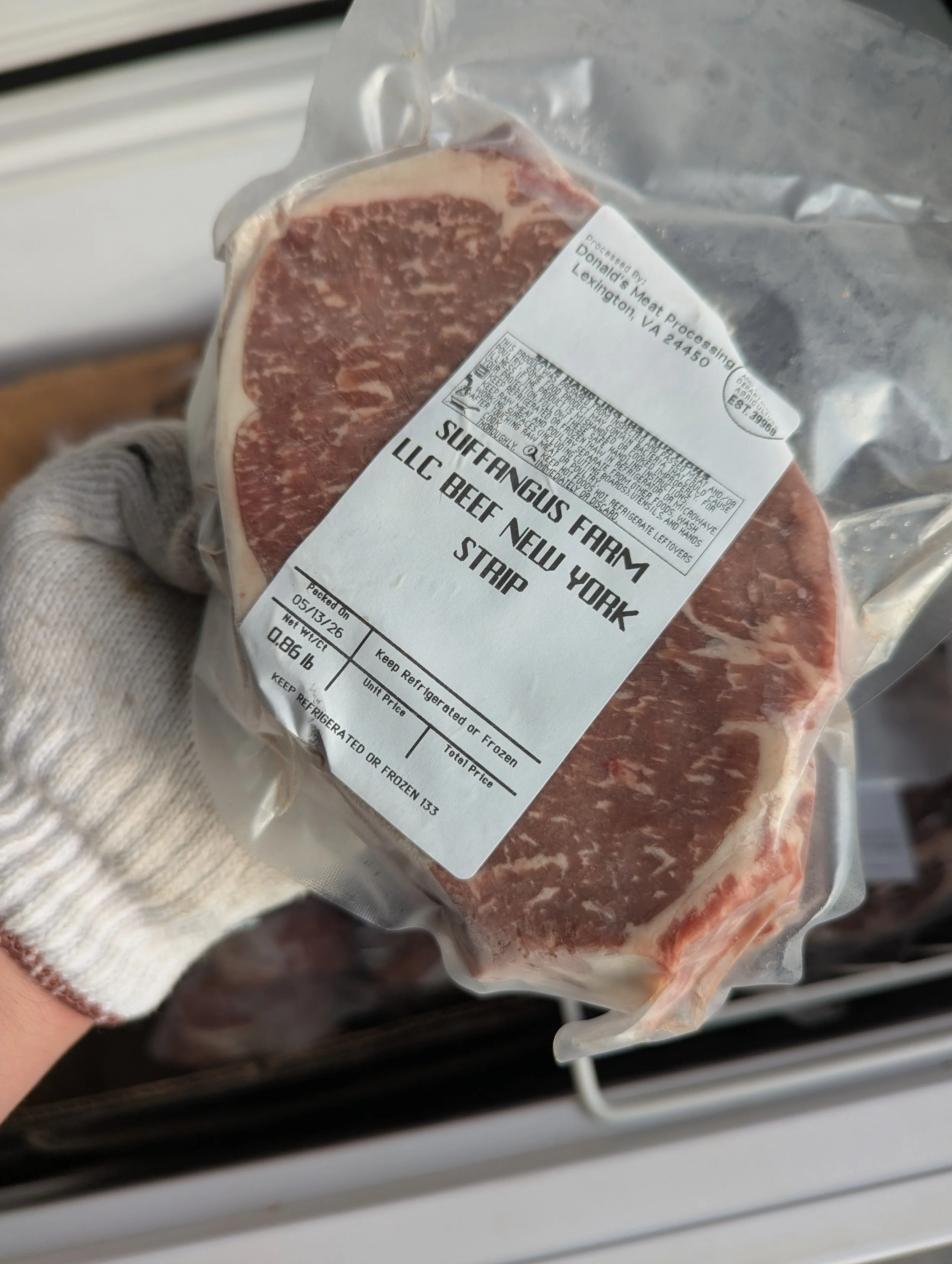 Frozen package of USDA certified Angus beef New York strip steak from Sullivan's Farm, Lexington, Virginia, being held in a gloved hand.