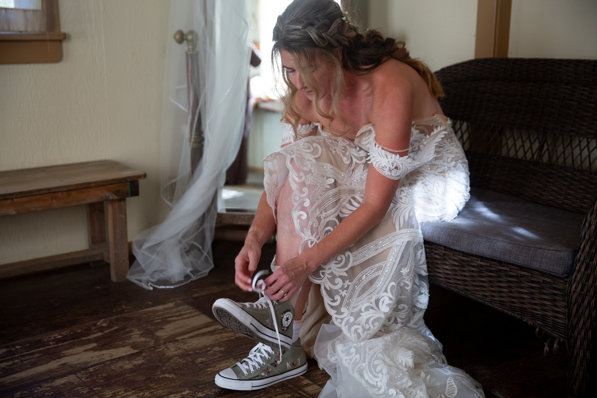 Bride in a lace wedding dress tying shoelaces on sneakers indoors.