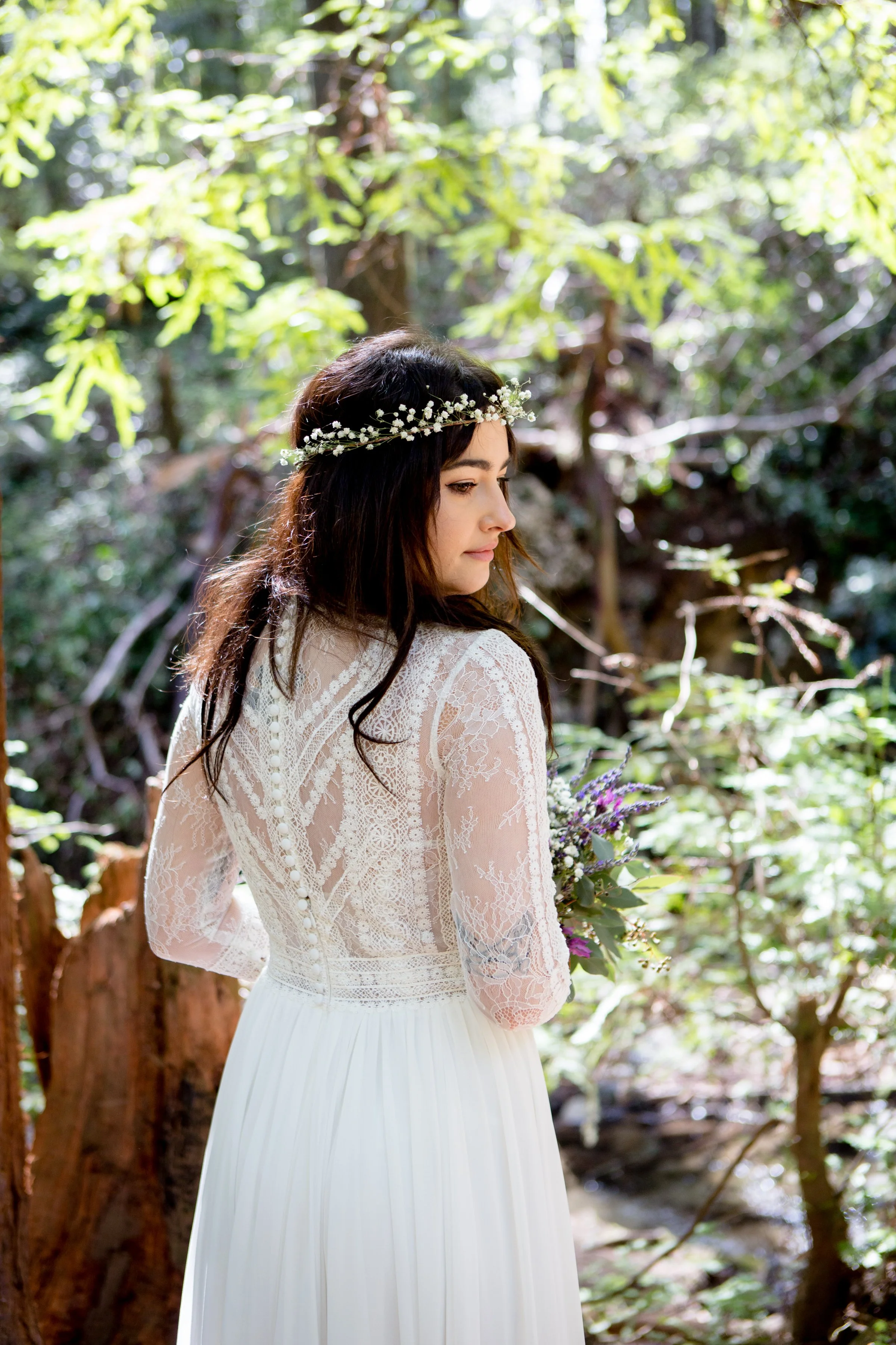 Bride in lace dress and floral crown standing in forest