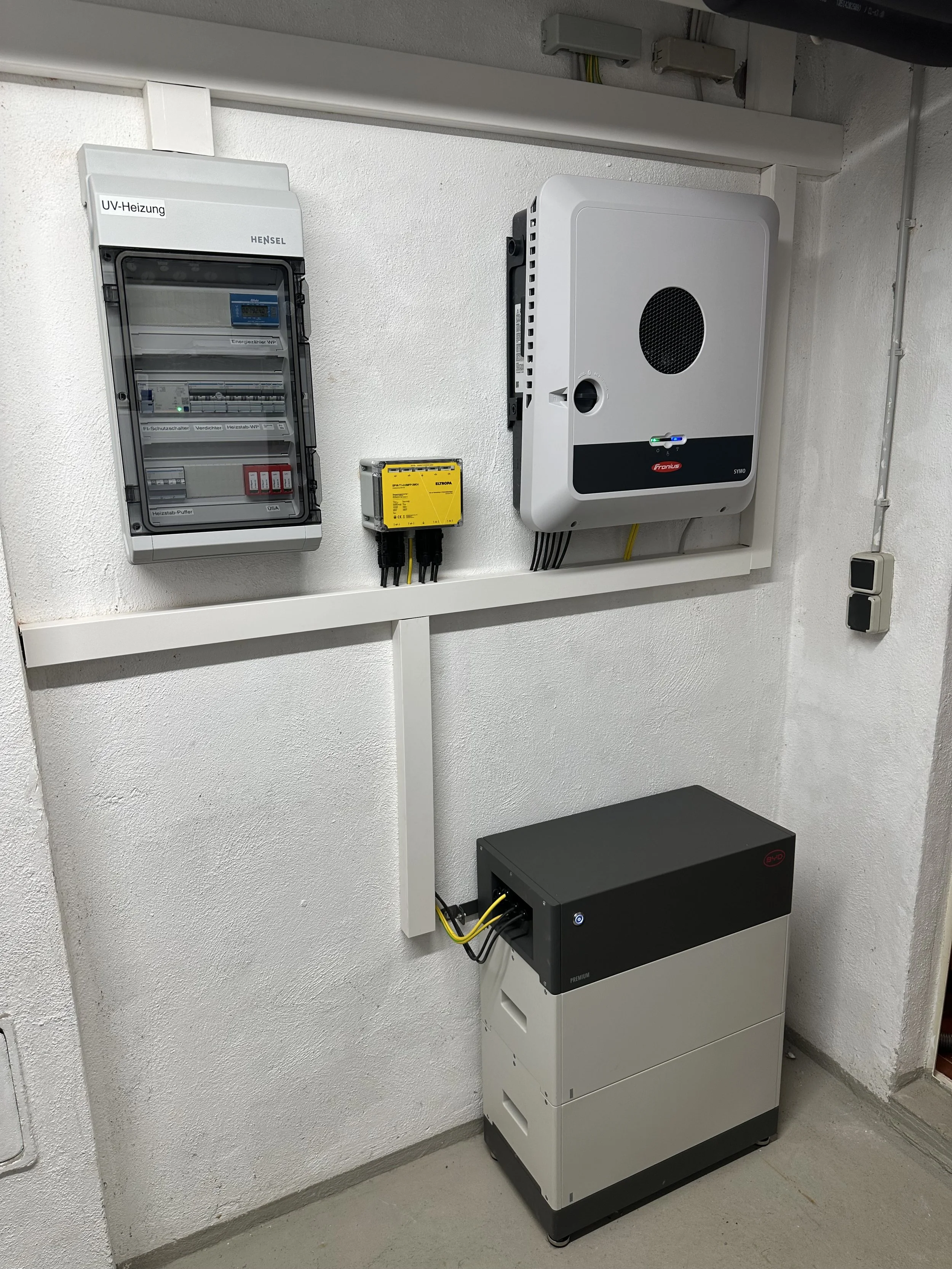 Ein Elektronikraum mit verschiedenen elektrischen Geräten, darunter ein Steuerkasten, ein Wechselrichter, eine Batterie, ein Steuergerät und eine Wandmontage.