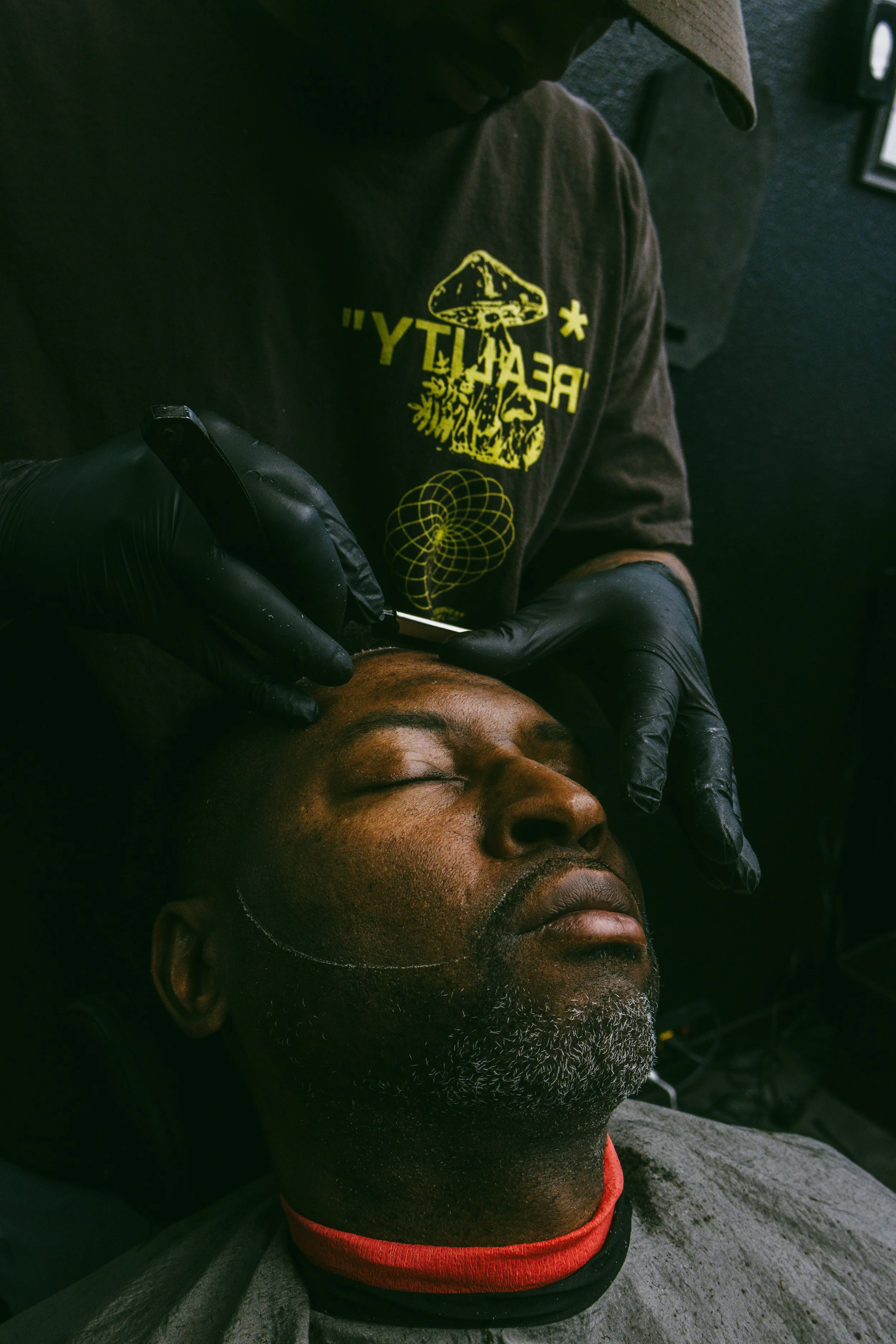 A man receiving a tattoo on his forehead from a tattoo artist wearing black gloves.