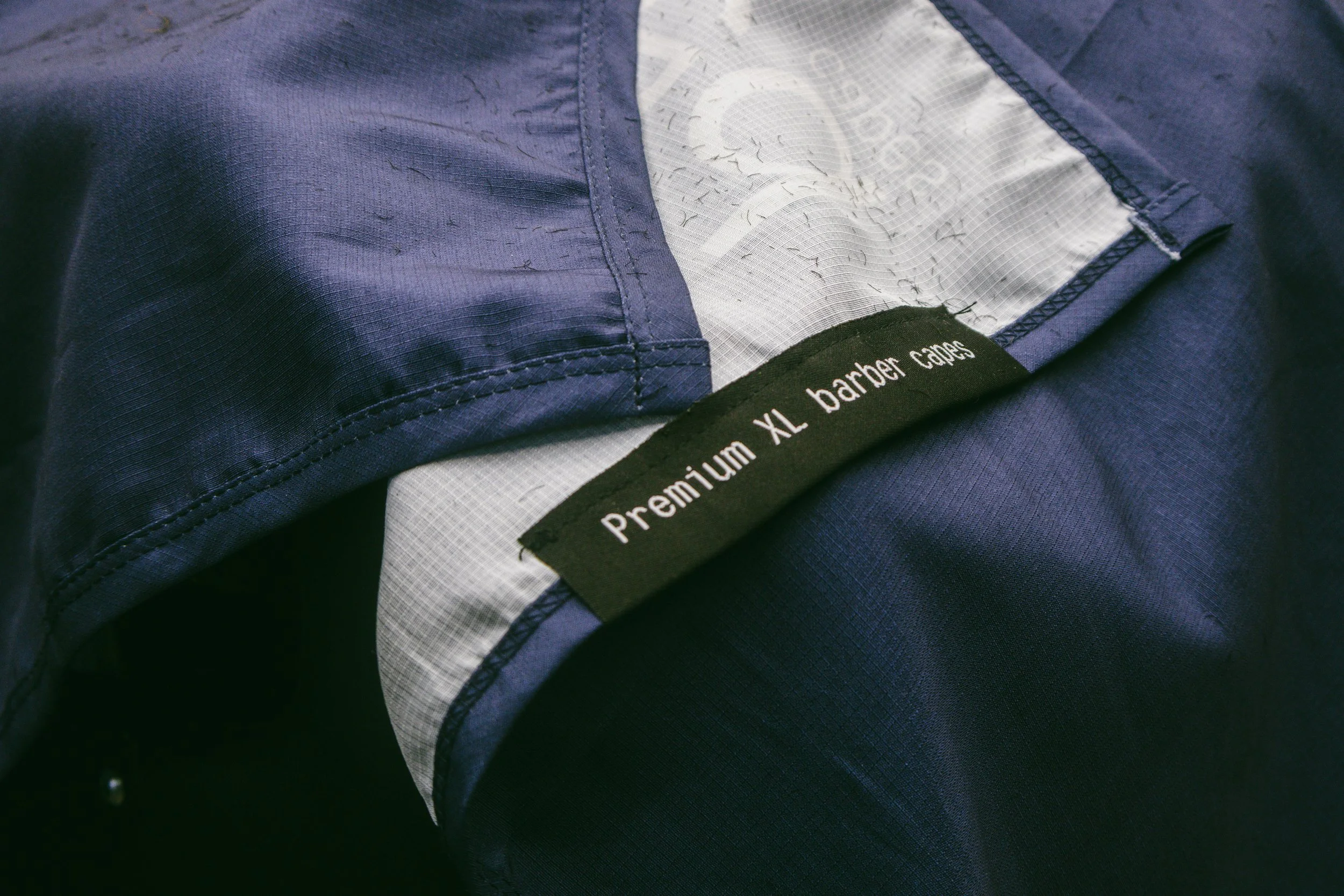 Close-up of a navy blue jacket with a black tag that reads 'Premium XL barber cape'.