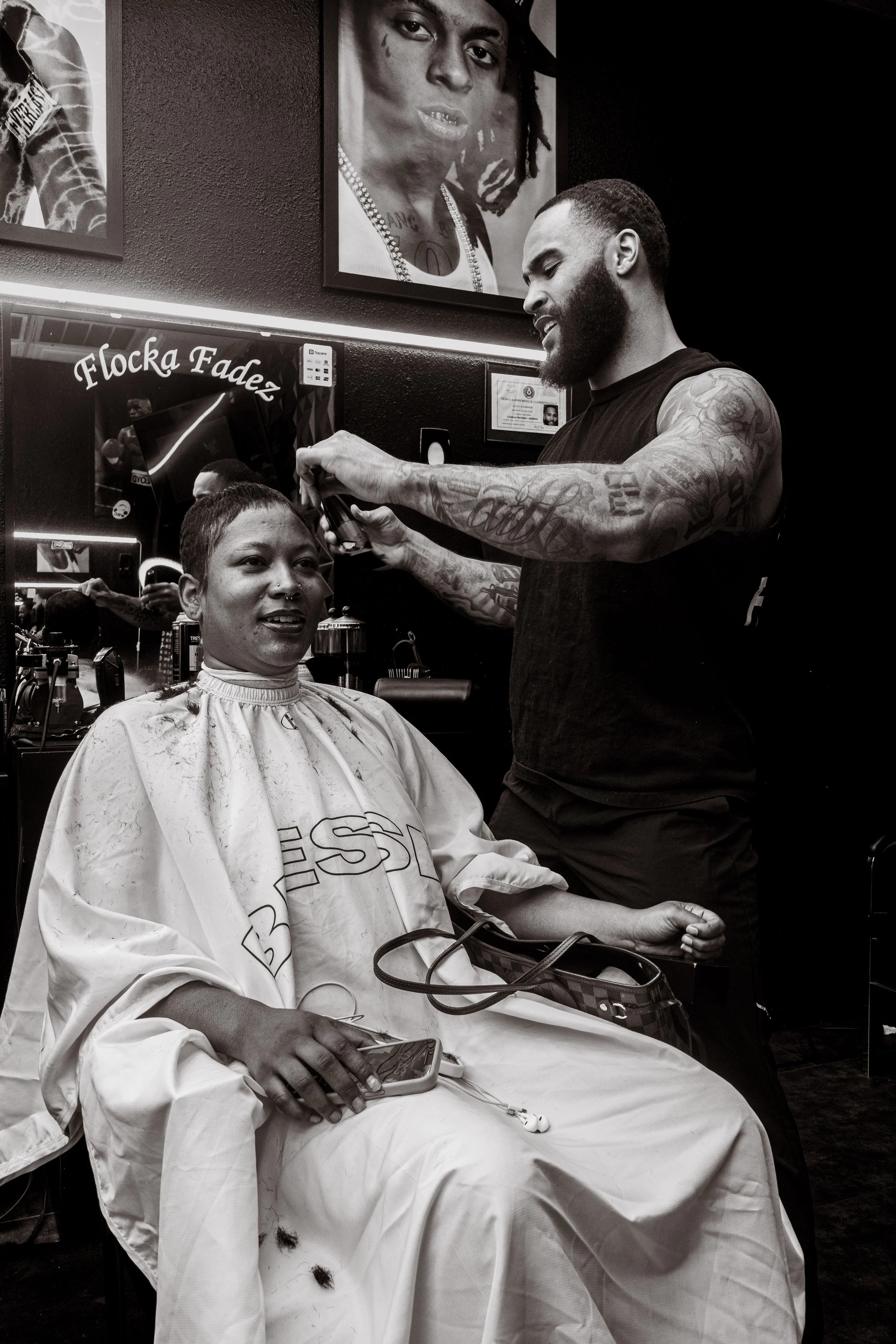 A woman getting a haircut at a barbershop, with a man cutting her hair, map, and picture of a woman with dreadlocks on the wall.