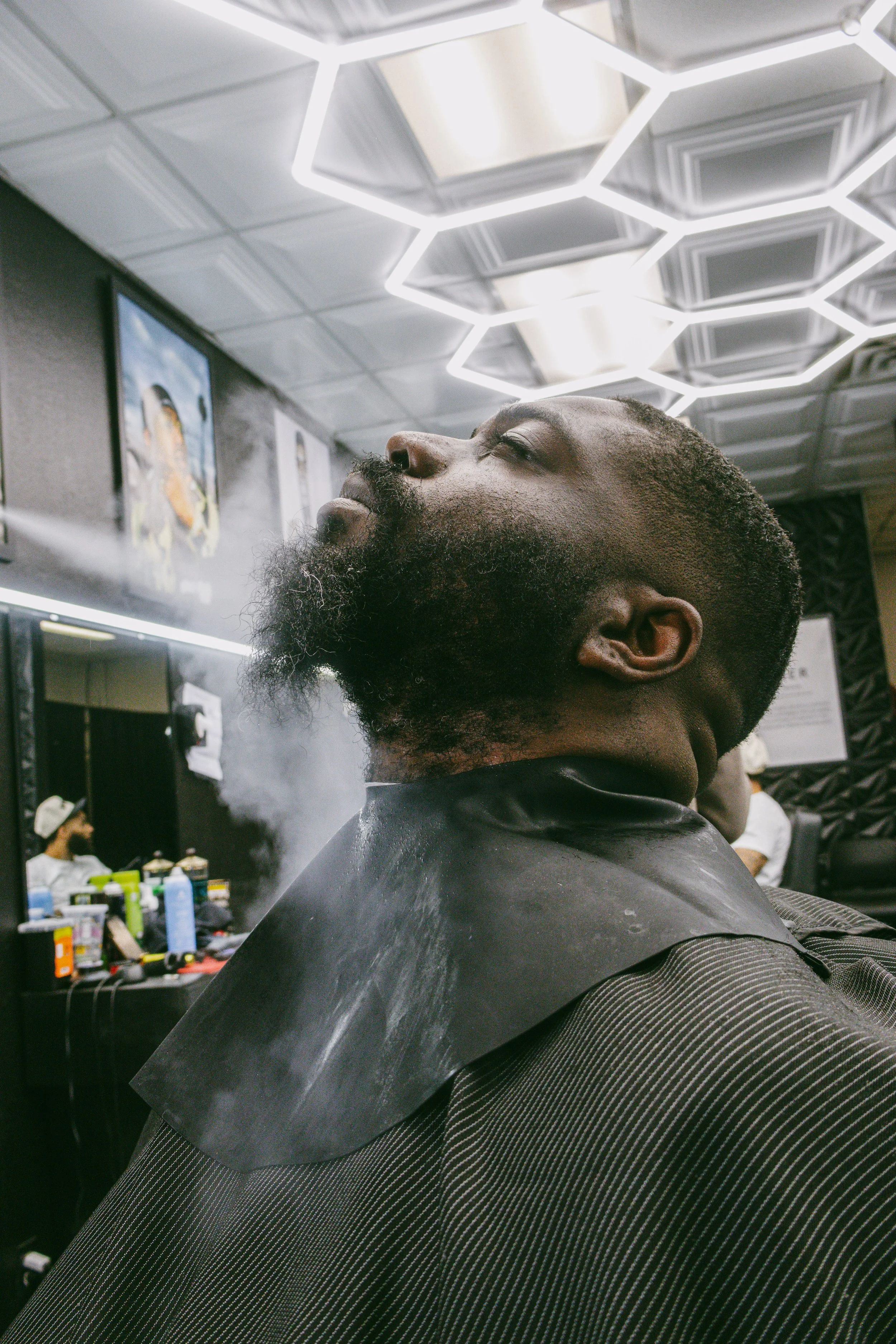 Man getting a straight razor shave at barbershop with steam and modern lighting.