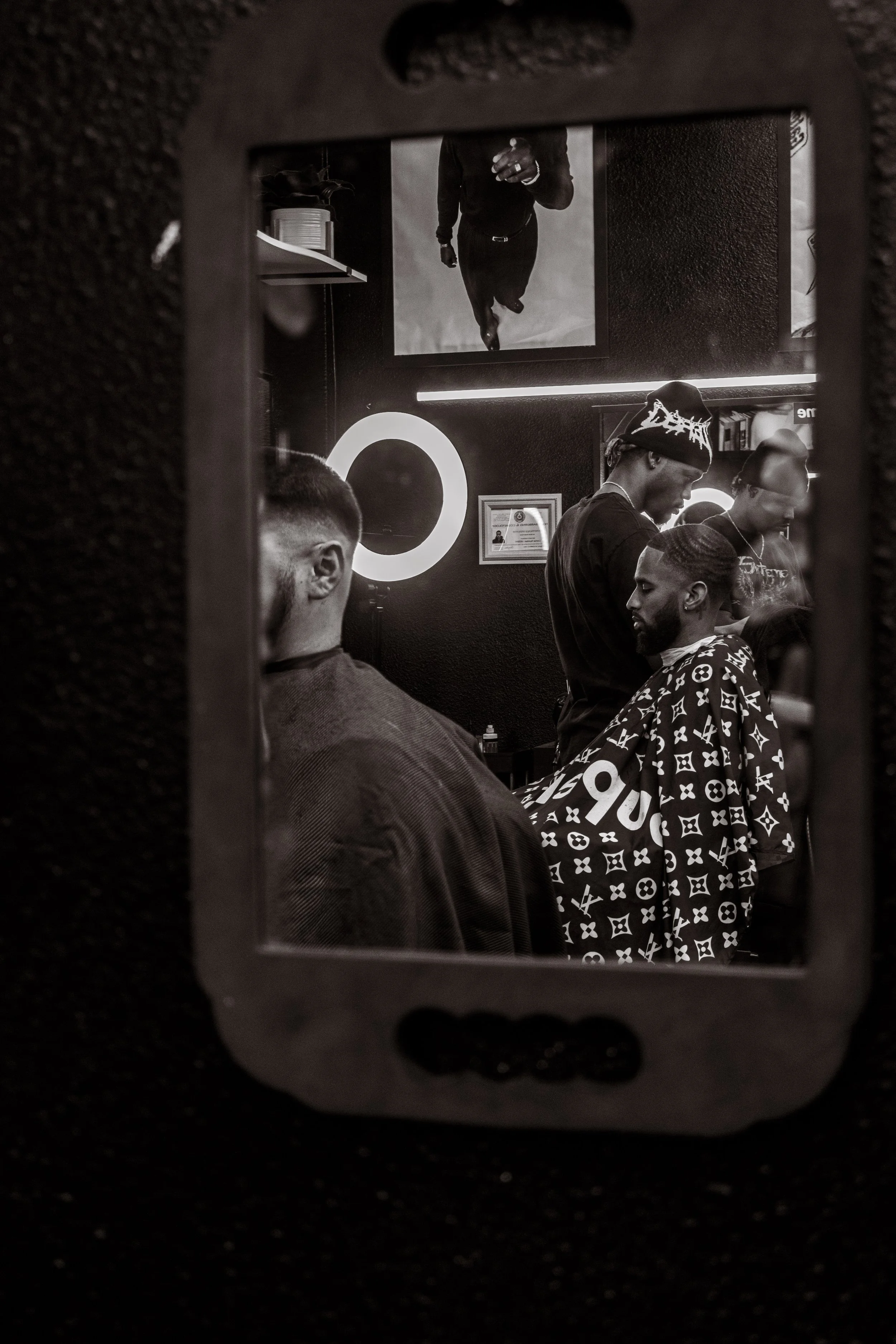 People getting haircuts in a barbershop as seen through a mirror reflection.