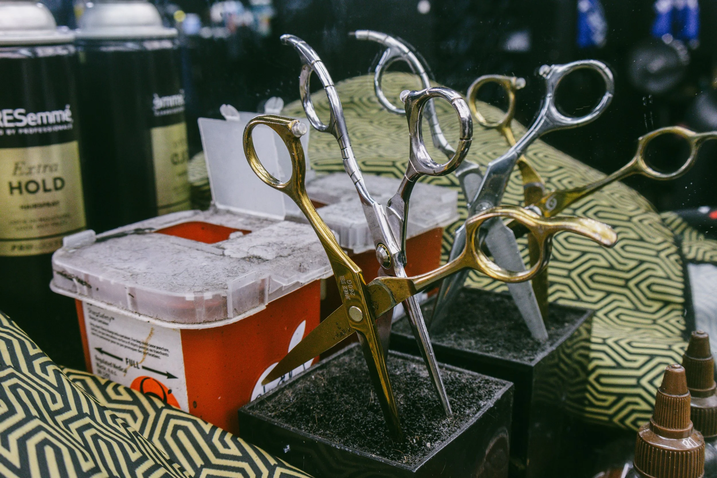 A display of various hairdressing scissors and tools on a table, with styling products in the background.