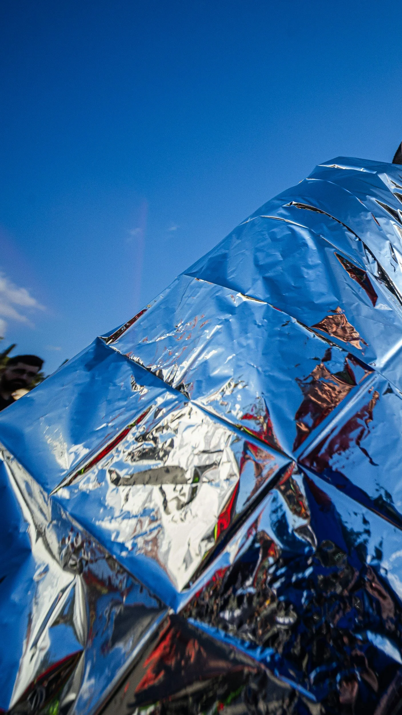 A row of objects wrapped in shiny aluminum foil under a clear blue sky.