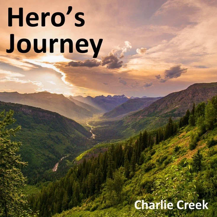 Scenic view of a green valley with mountains and a creek, under a sunset sky, with the text 'Hero's Journey' and 'Charlie Creek'.