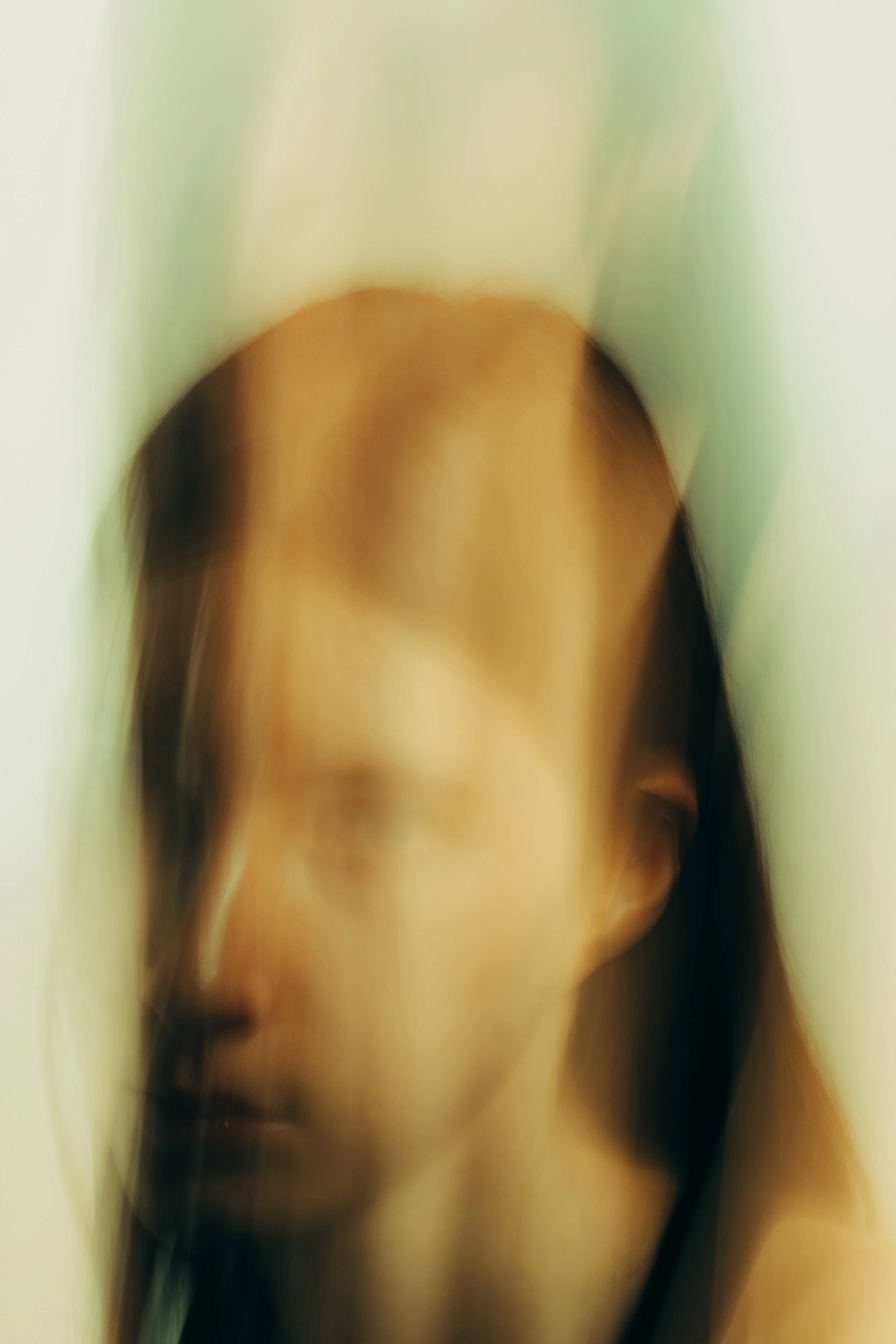 A blurred close-up of a person's face, with long dark hair, partly obscured.