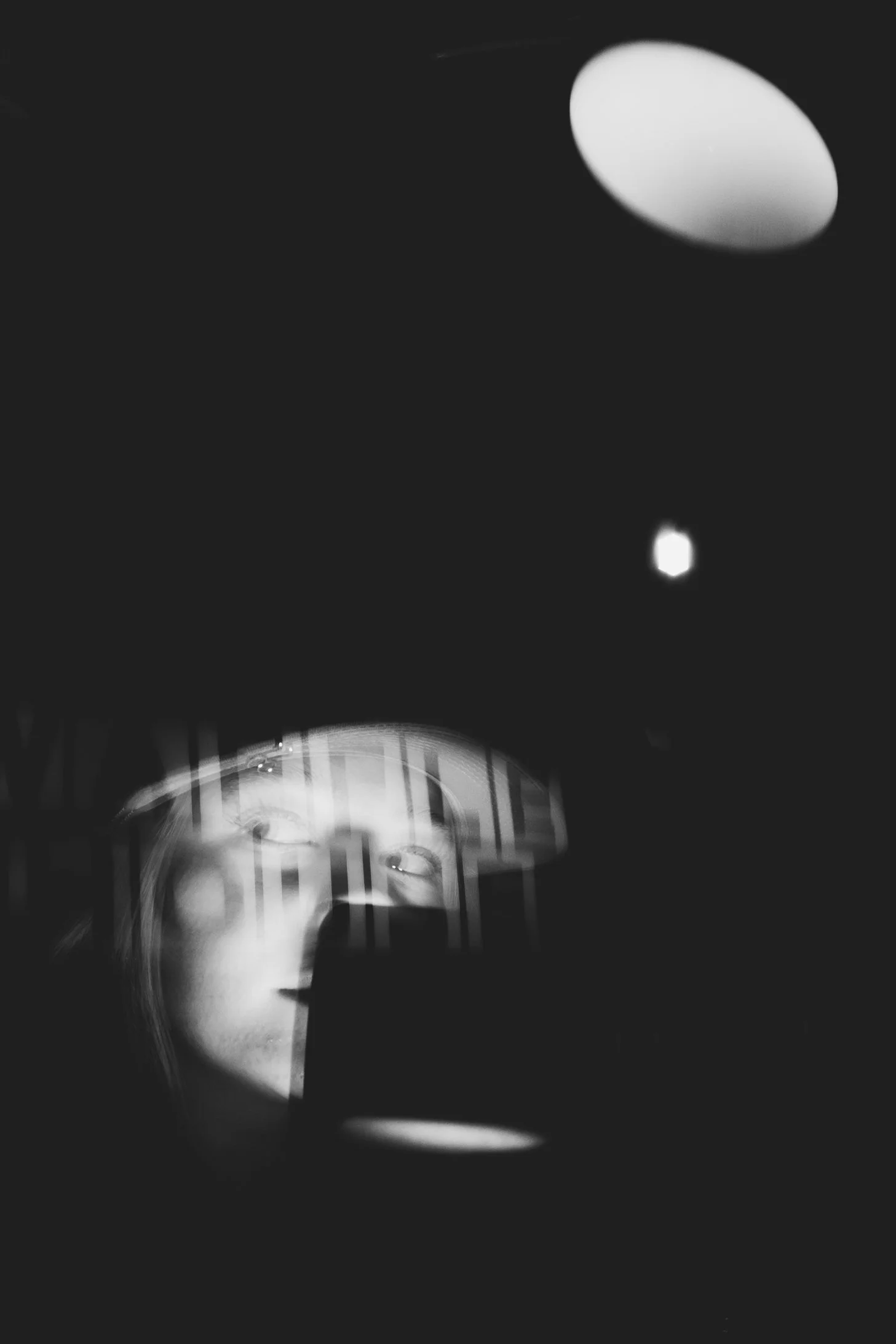 Abstract black and white photograph of a ceiling with light fixtures, including one bright oval light and multiple circular lamps