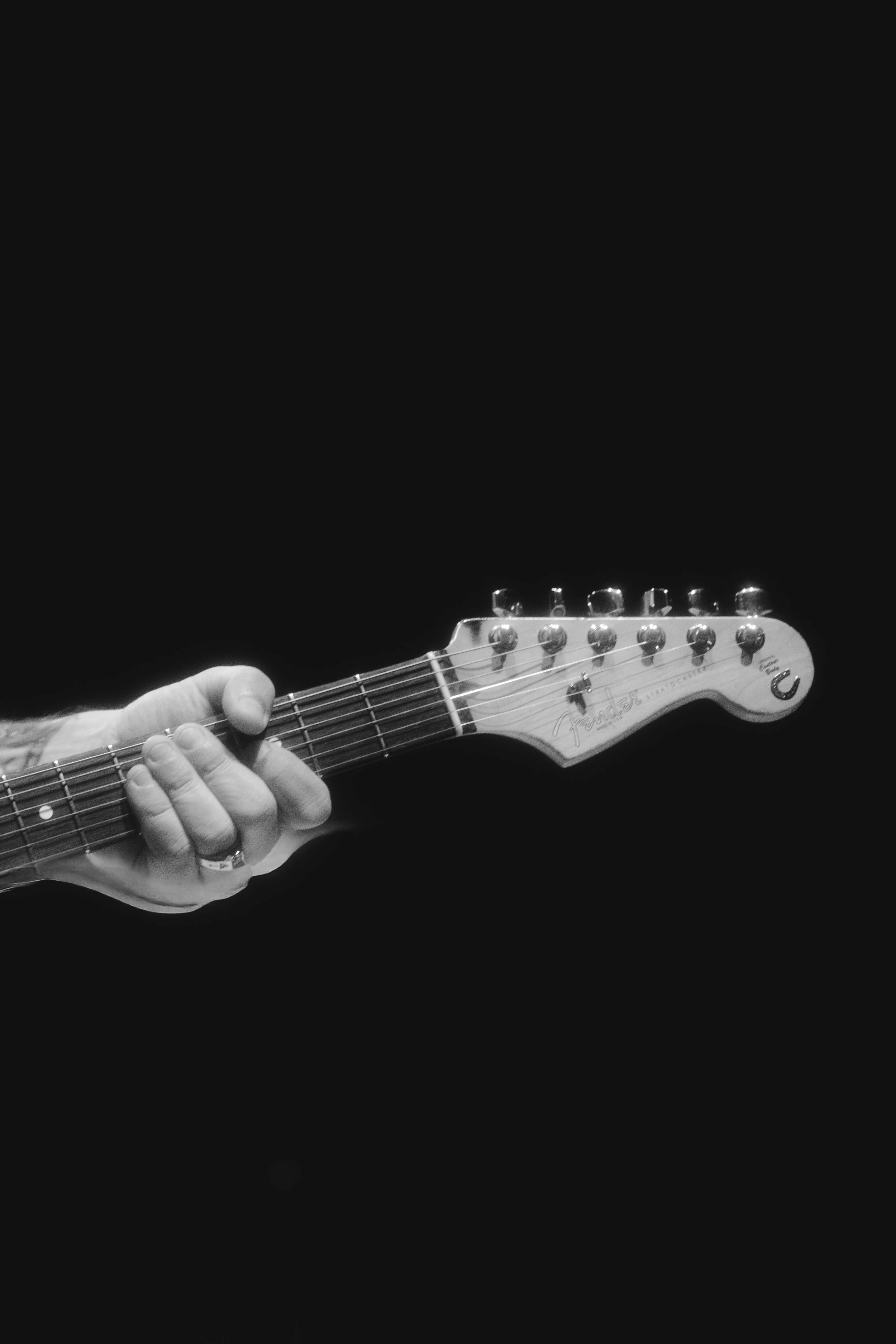 Close-up of a person's hand playing an electric guitar against a black background.
