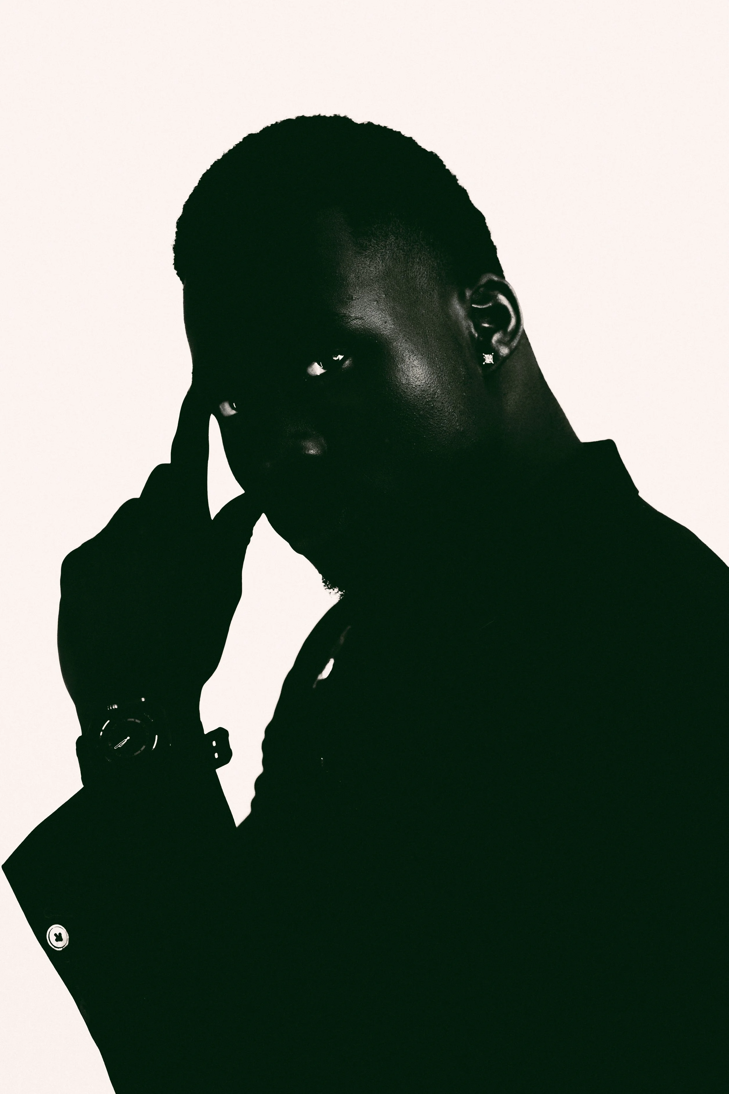 Silhouette of a person with short hair, holding a phone to their ear, wearing a watch and earrings, against a plain background.