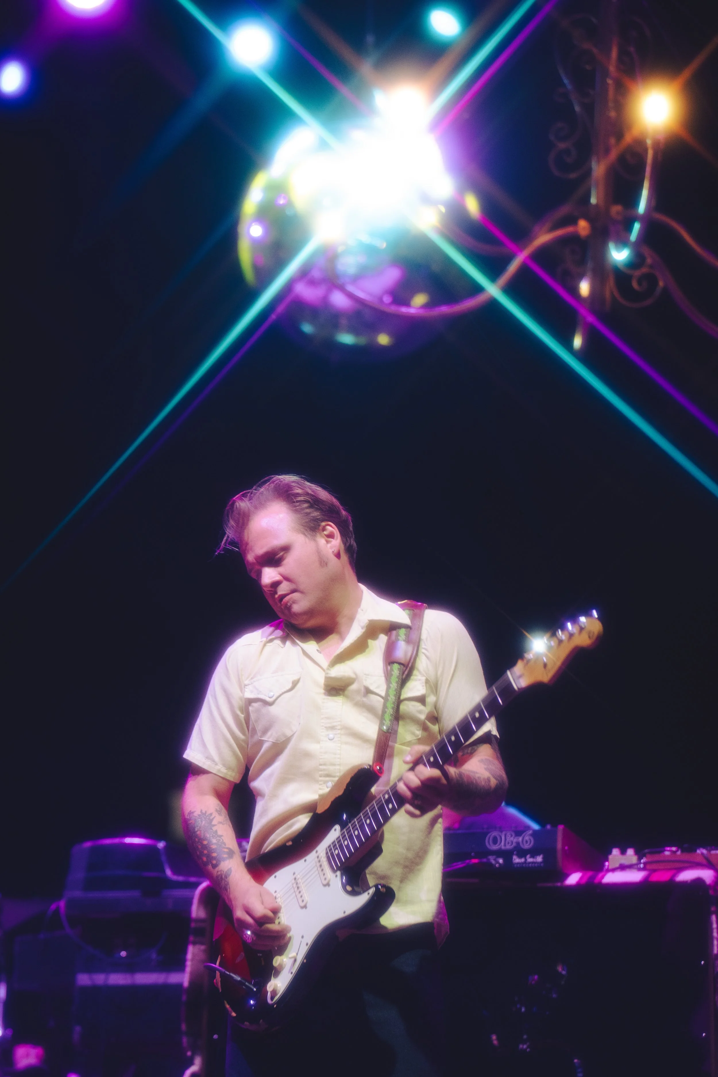 A man playing an electric guitar on stage under colorful stage lights.