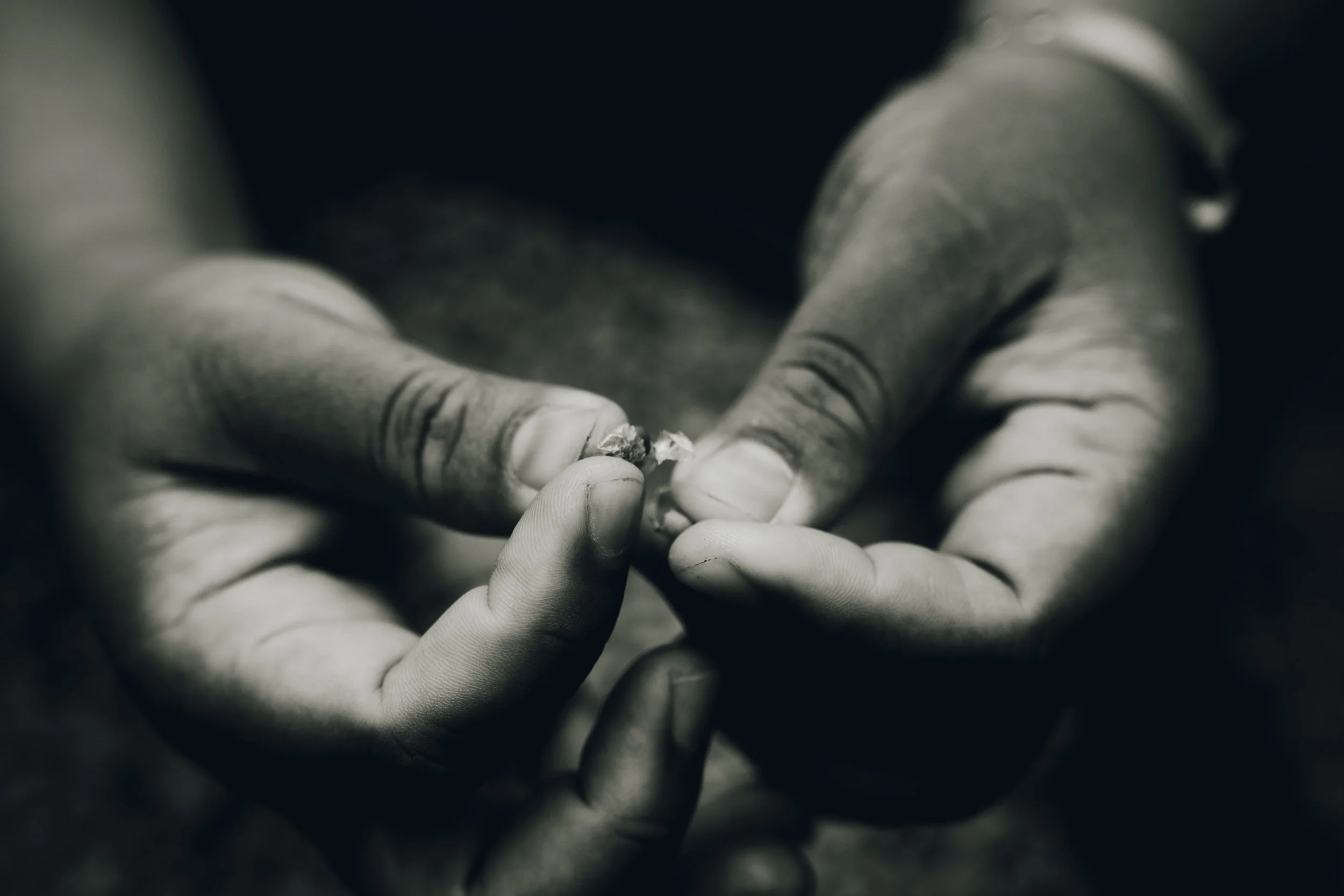 Close-up of hands and fingers holding and working on a small object in black and white.