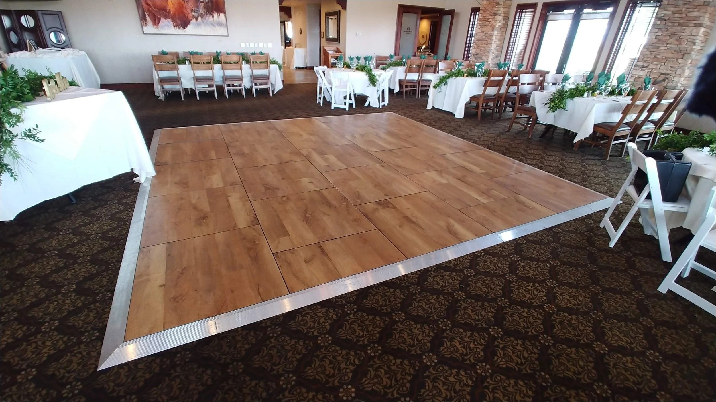 Empty wooden dance floor in a decorated banquet hall area with round tables and chairs, green napkins, and various decorations.
