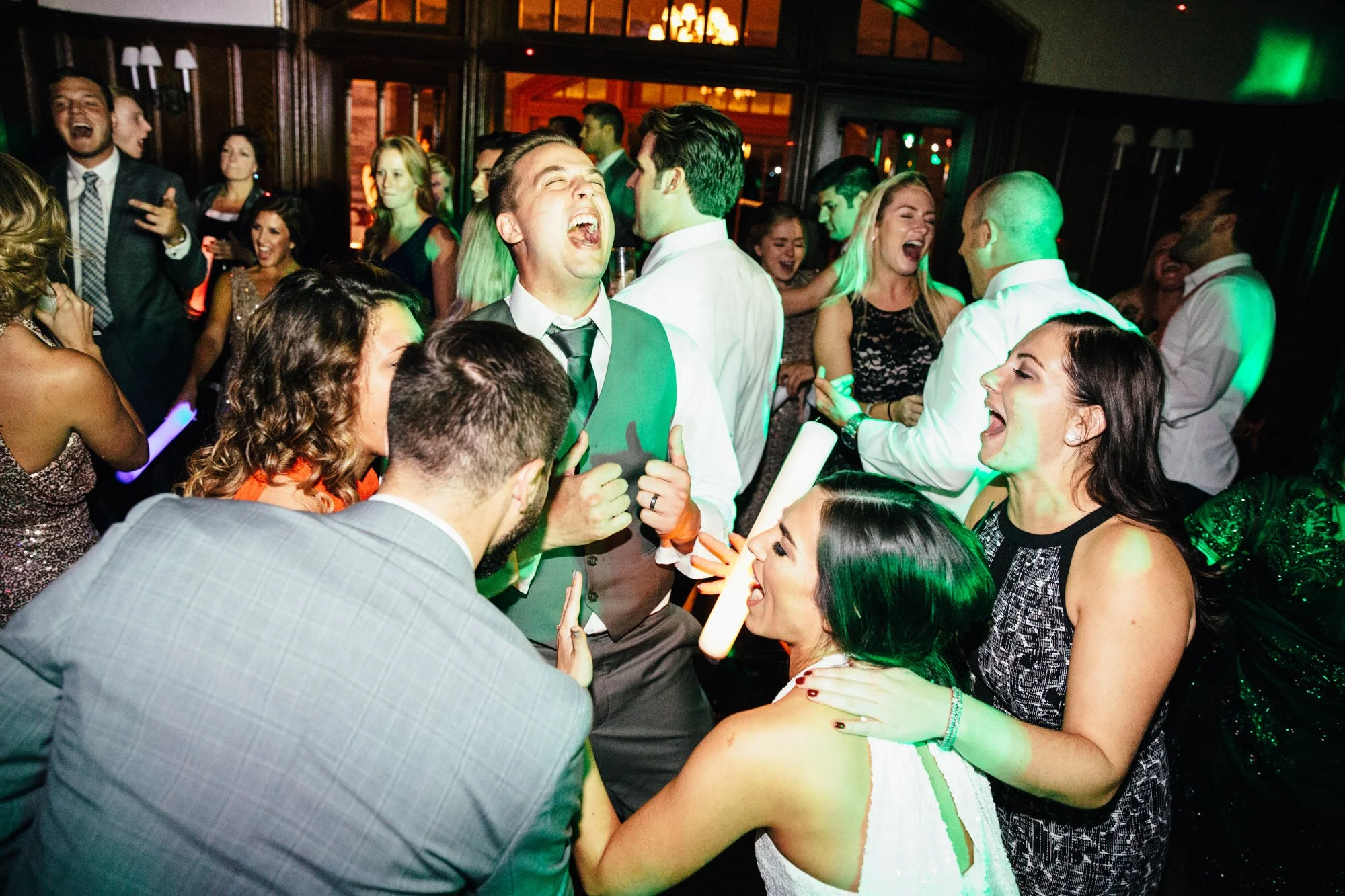 Group of people dancing and laughing at a lively indoor party or wedding reception.