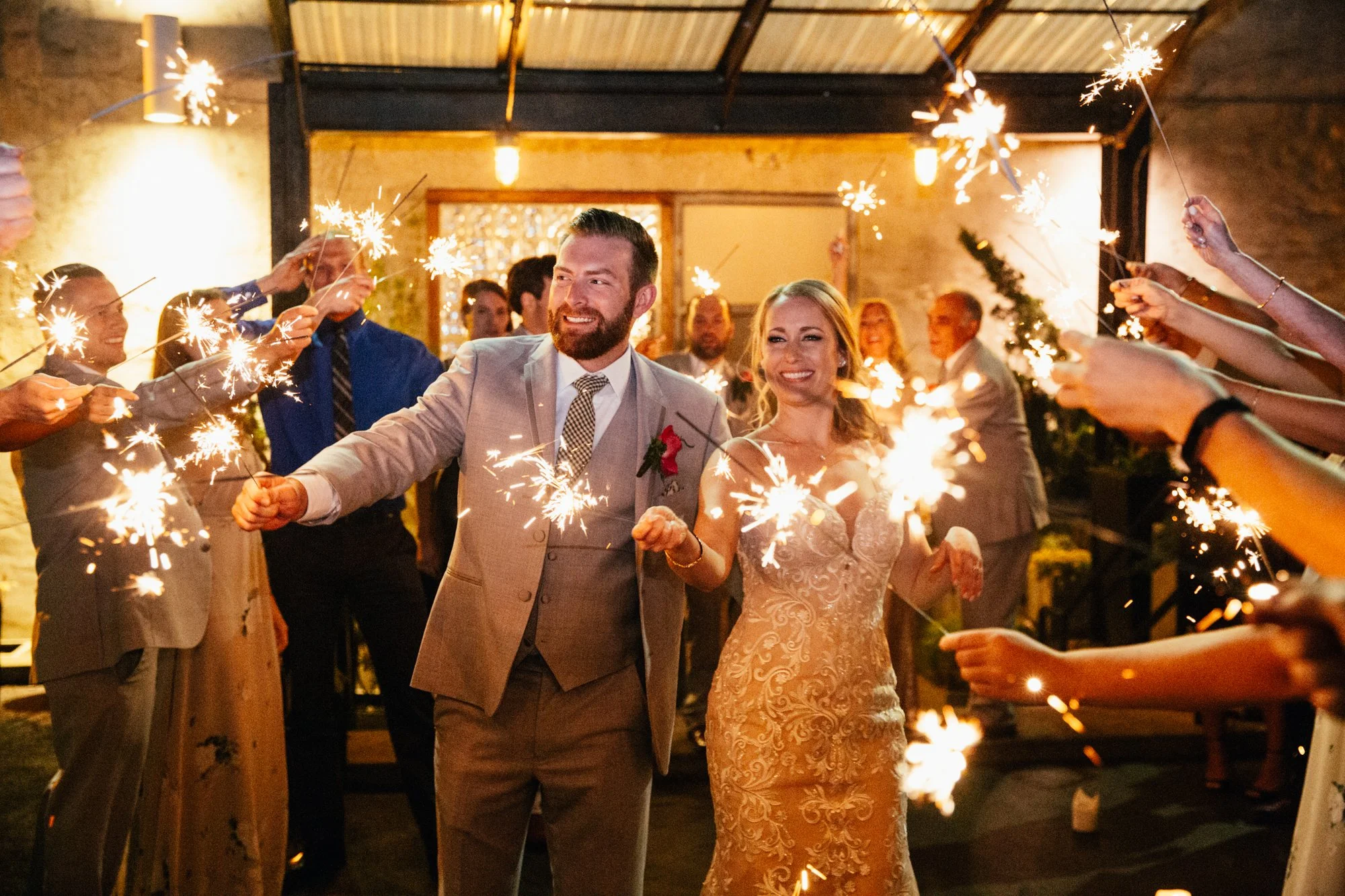 Bride and groom walking through guests holding sparklers at wedding.