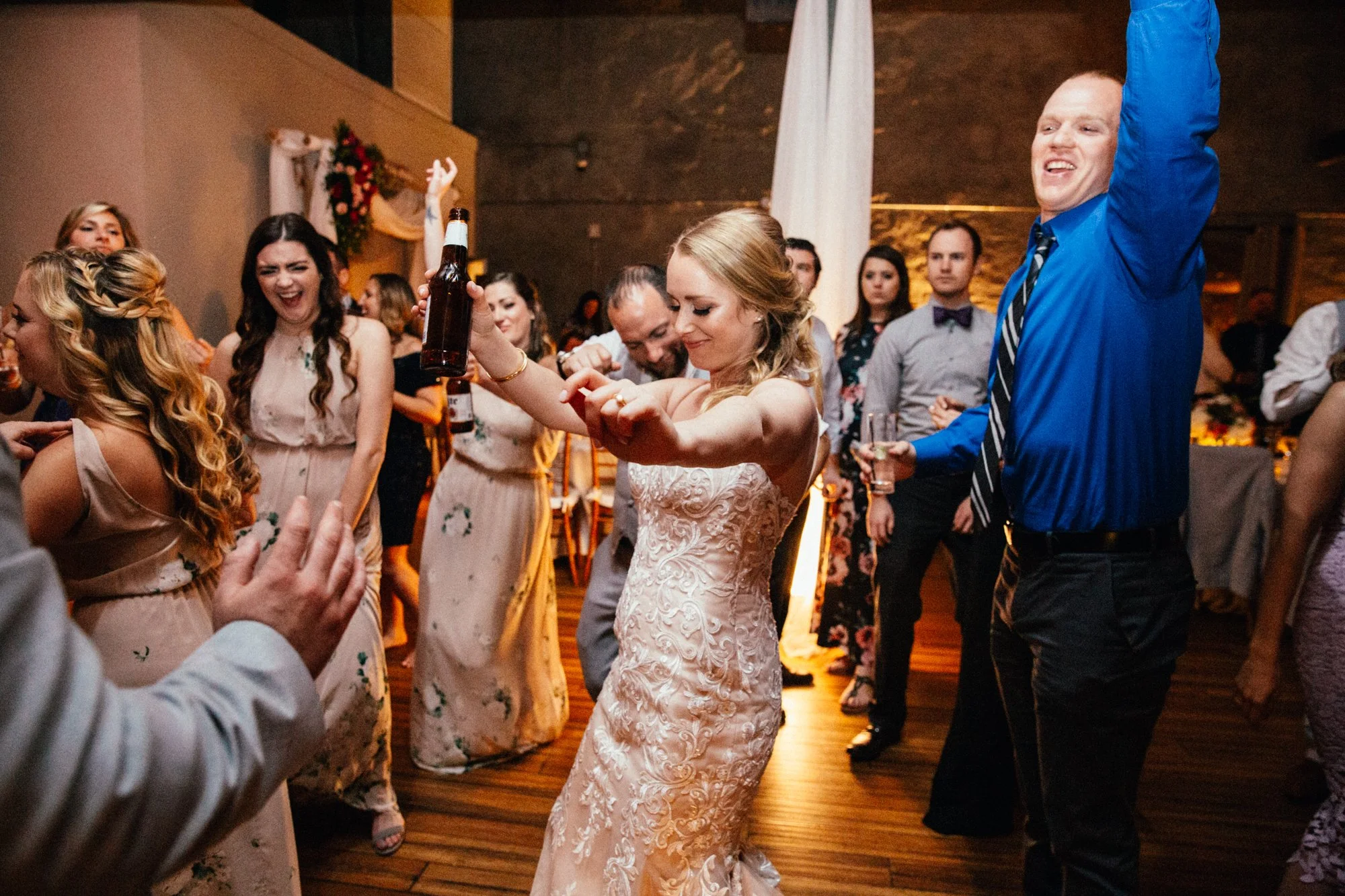 Wedding reception with guests dancing energetically, including a bride in a white dress and people holding drinks.