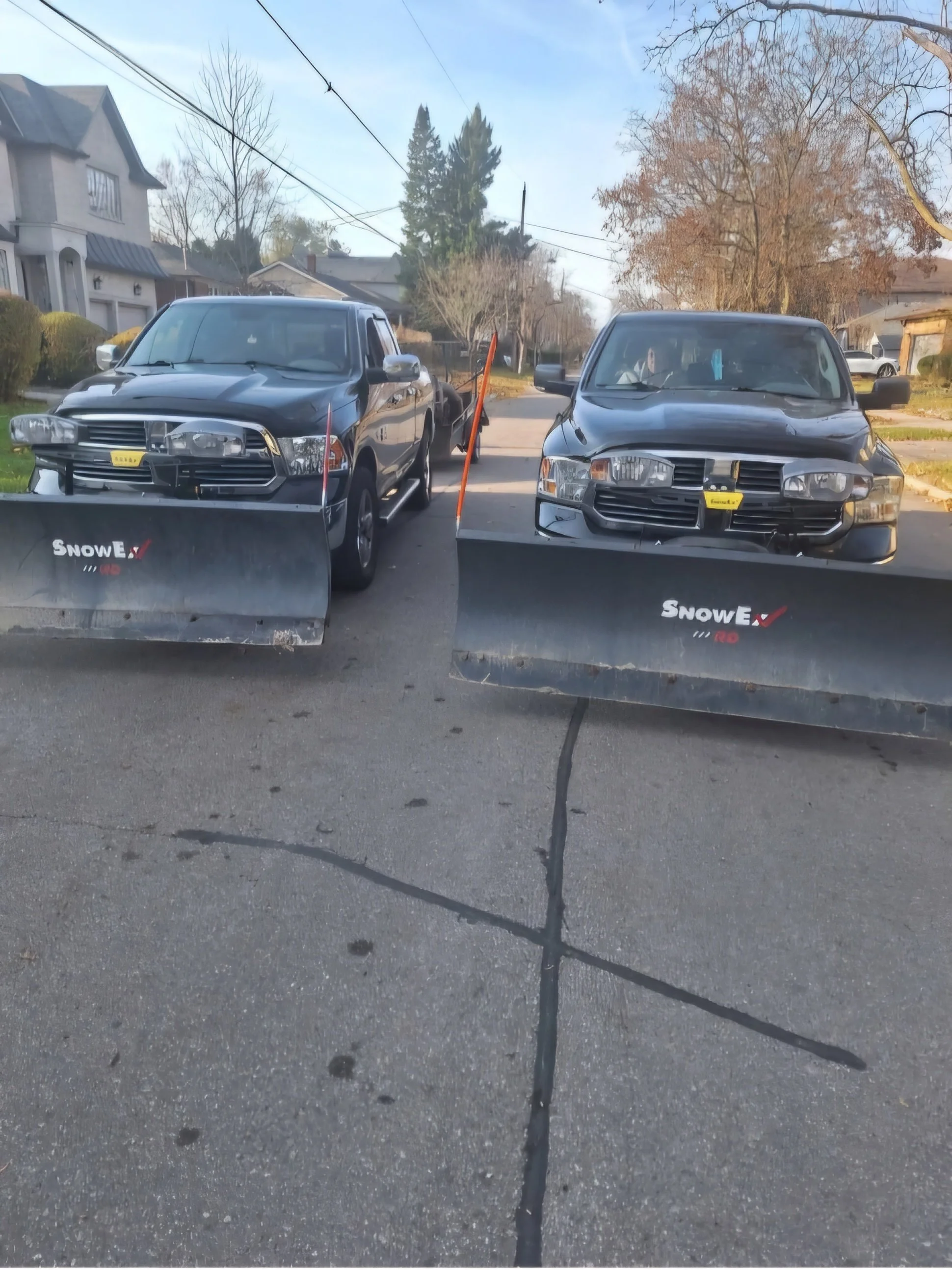 Two trucks equipped with snow plows parked on a residential street.