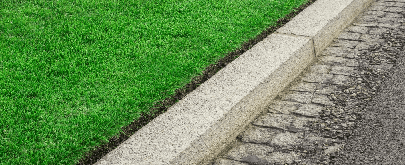 Grass lawn adjacent to a concrete curb and cobblestone street.