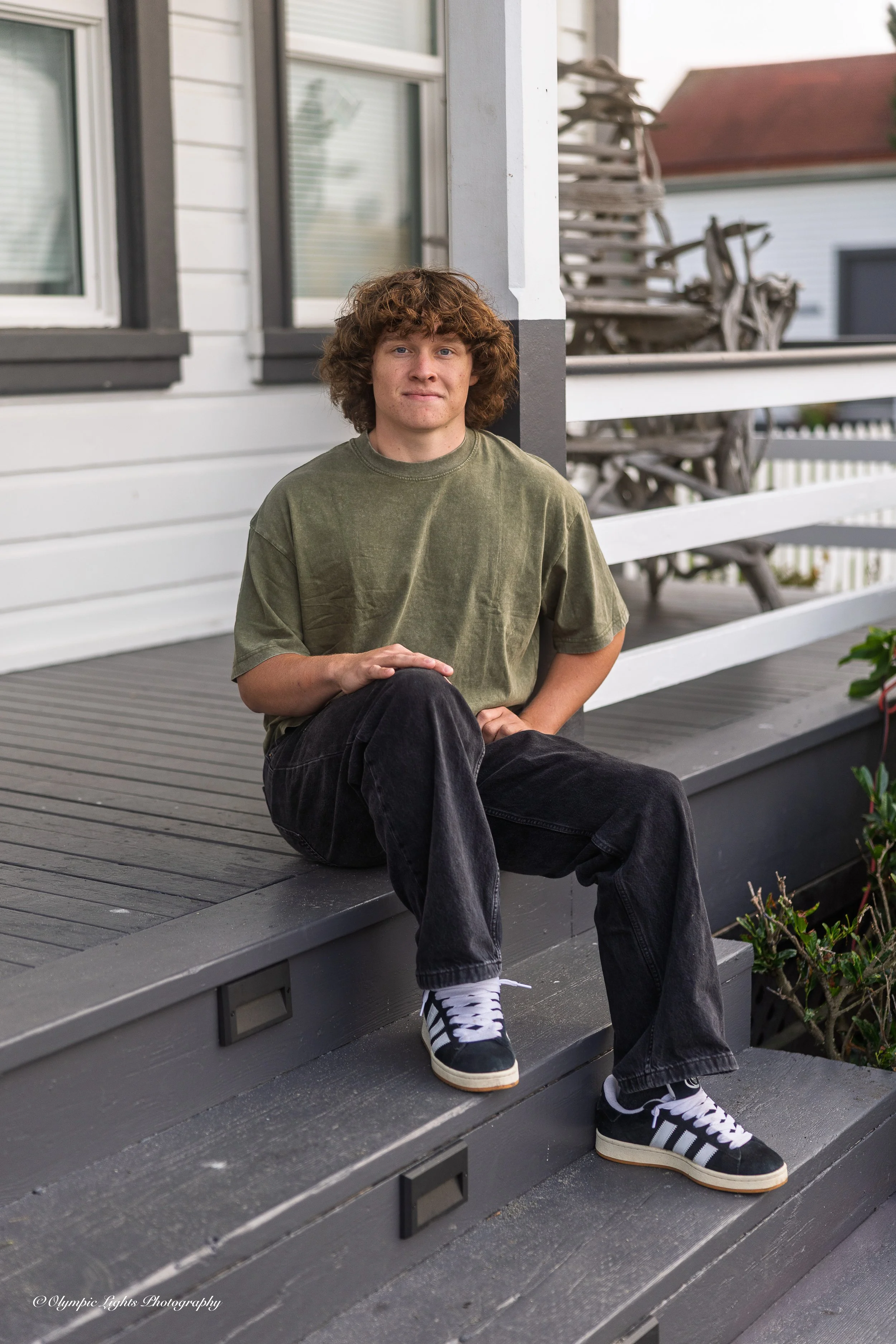 Young man with curly hair sitting on the porch steps of a house.