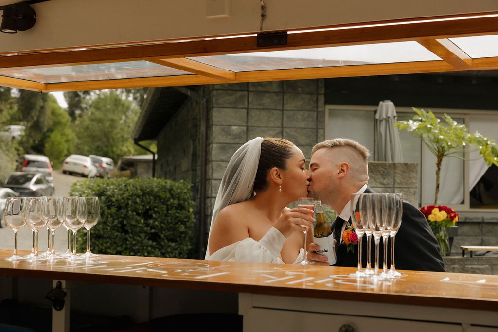 Newlywed couple sharing a kiss at the bar during their Waipuna Estate wedding