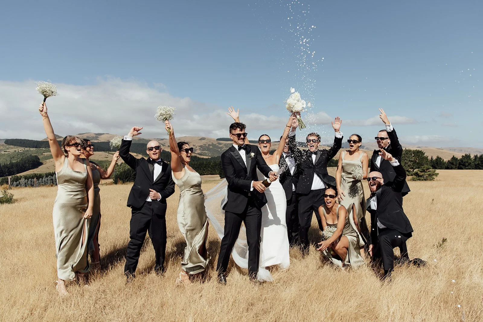 Wedding couple celebrating with their bridal party in the open fields at Waipuna Estate
