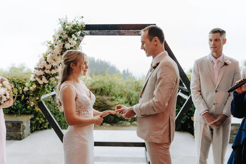 Bride and groom exchanging vows during an intimate outdoor wedding ceremony surrounded by floral arrangements at Waipuna Estate