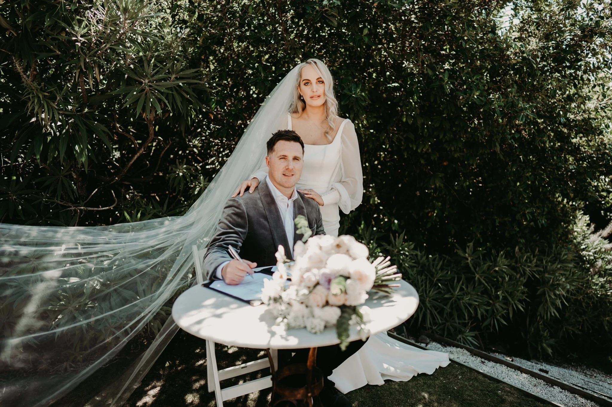 Bride and groom sharing an intimate wedding signing moment surrounded by lush greenery at Waipuna Estate