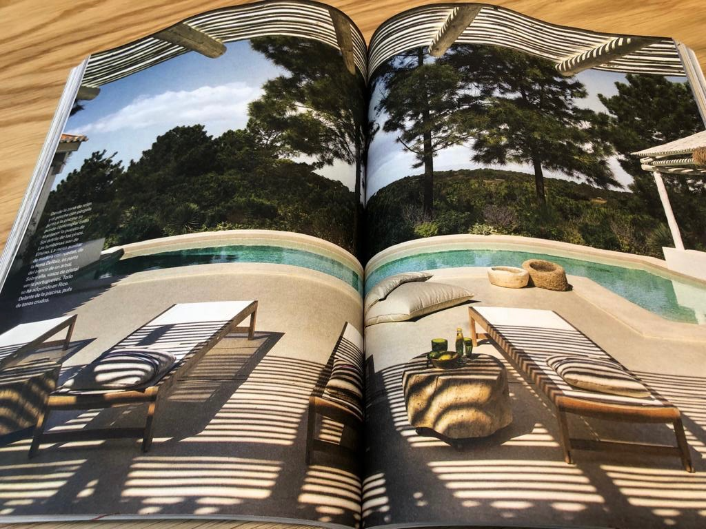 A magazine open to a page showing a backyard with a swimming pool, lounge chairs, cushions, and trees in the background.